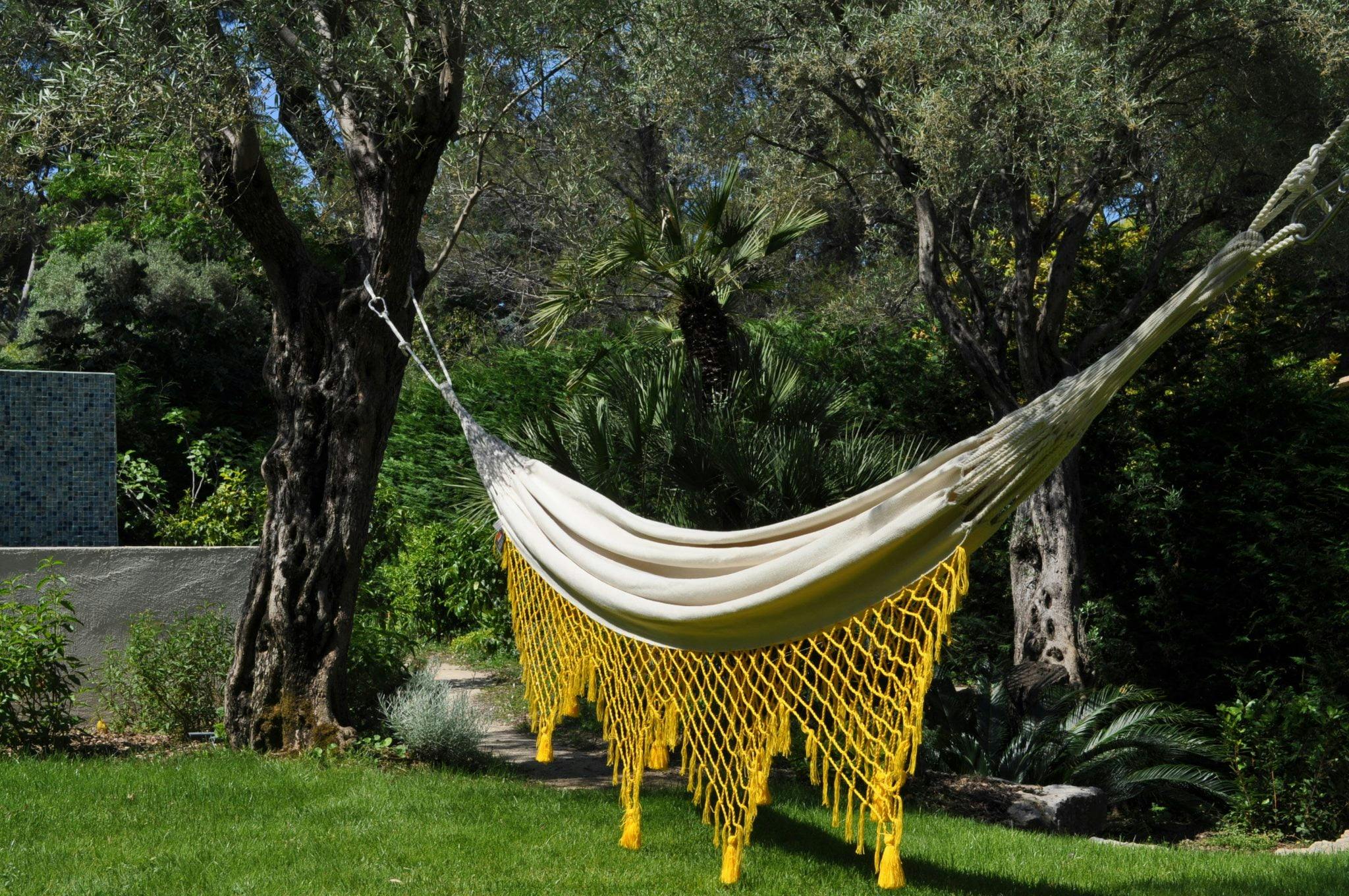 Hammock with yellow net suspended between two tree trunks in the garden, above the green lawn