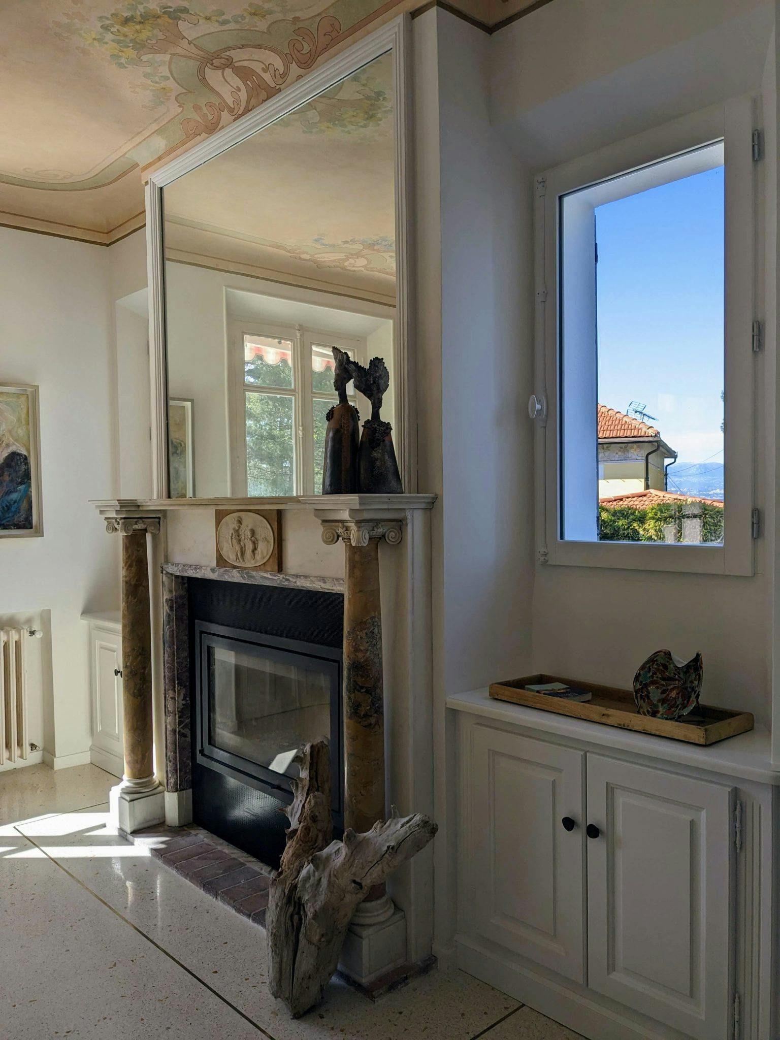 In the living room: antique marble fireplace with mirror above, window overlooking the outdoors