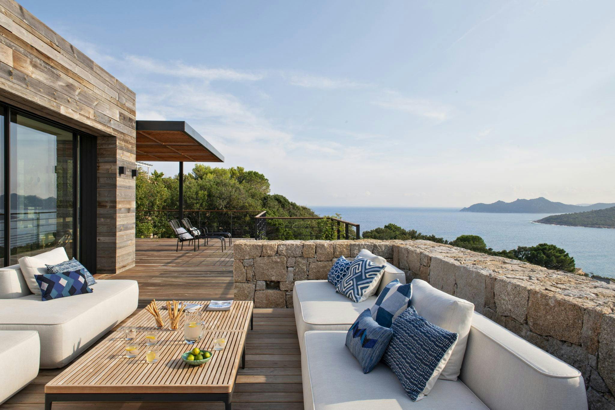 terrasse en bois avec rambarde en pierre, les canapés de la villa disposent d'une vue sur la mer