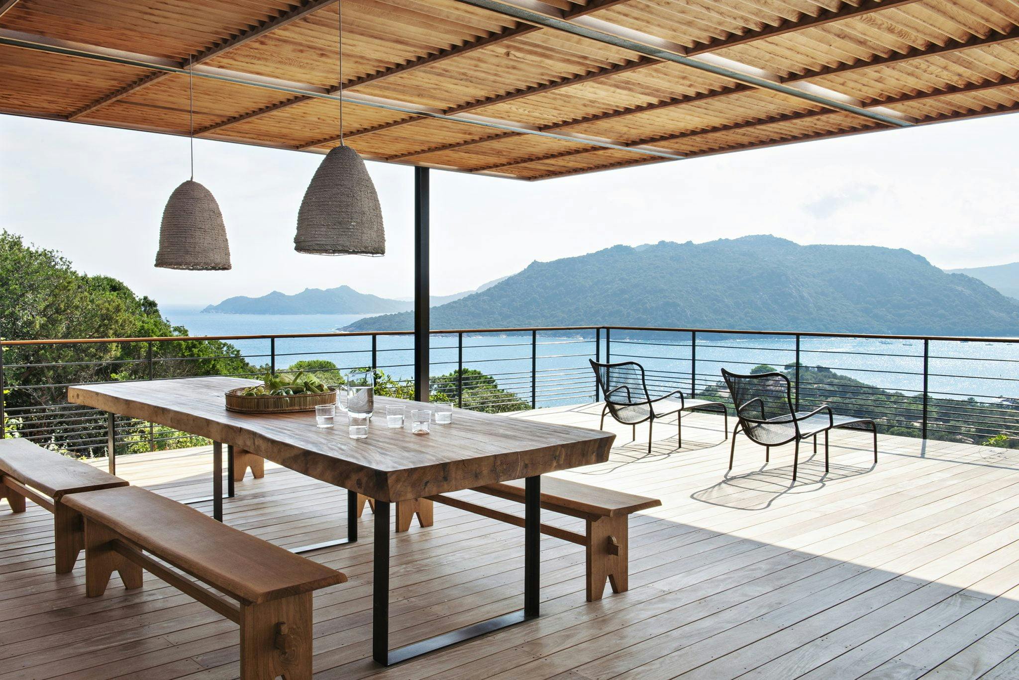 terrasse couverte vue sur la mer, disposant d'une grande table et de luminaires suspendus