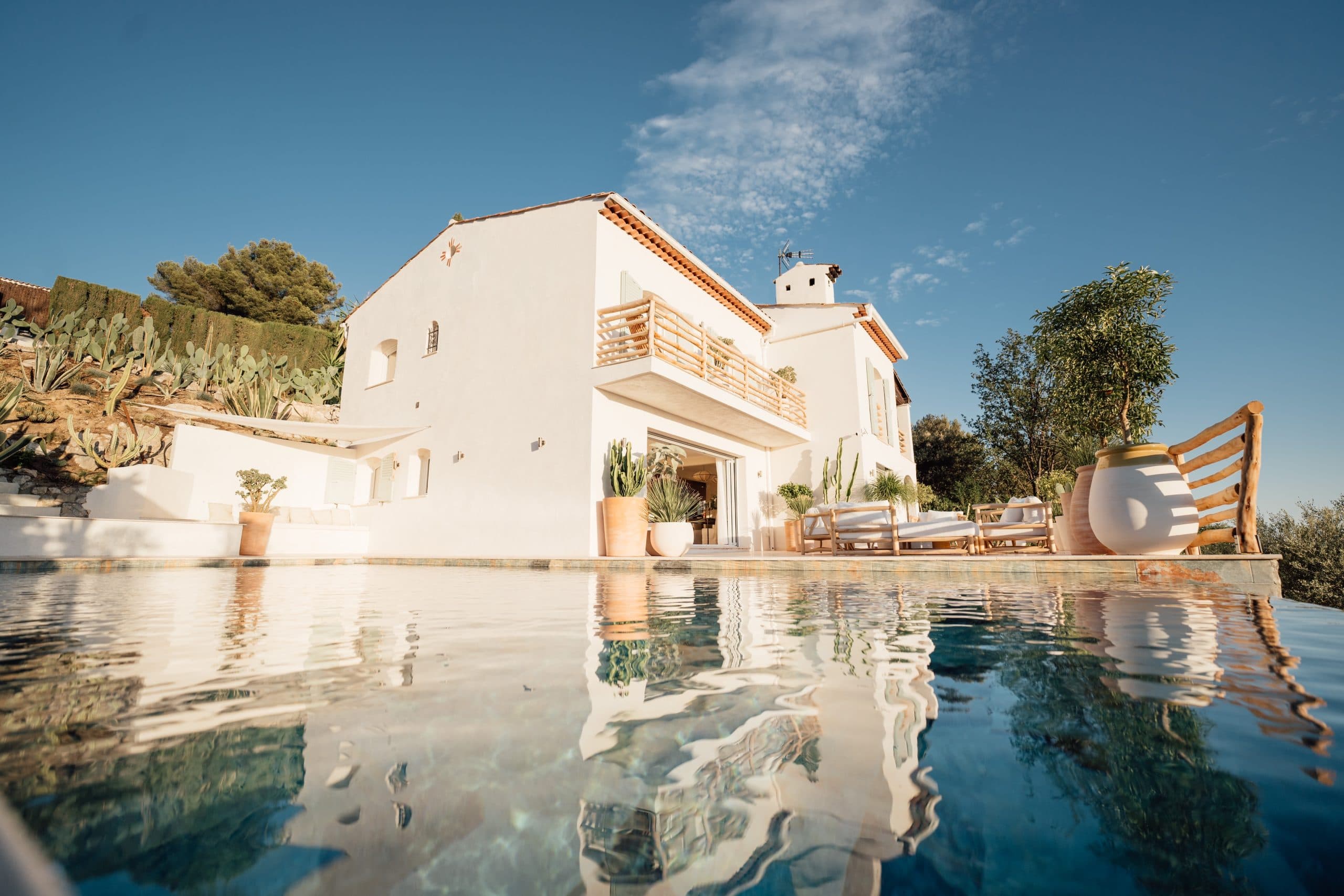Vue sur la maison depuis l'eau de la piscine, qui reflète les couleurs blanches