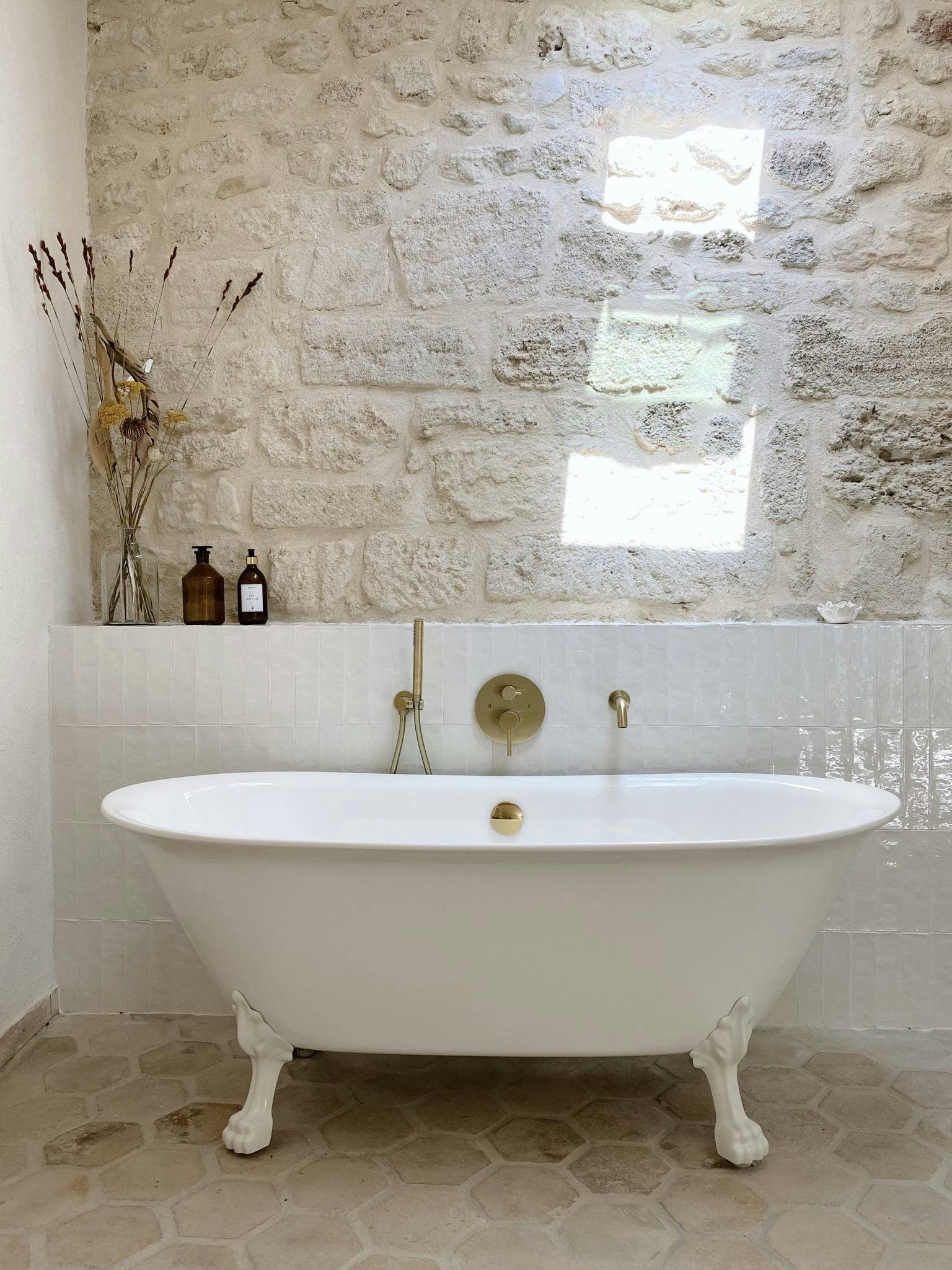 Free-standing bathtub in front of a half-height tiled wall and a stone wall