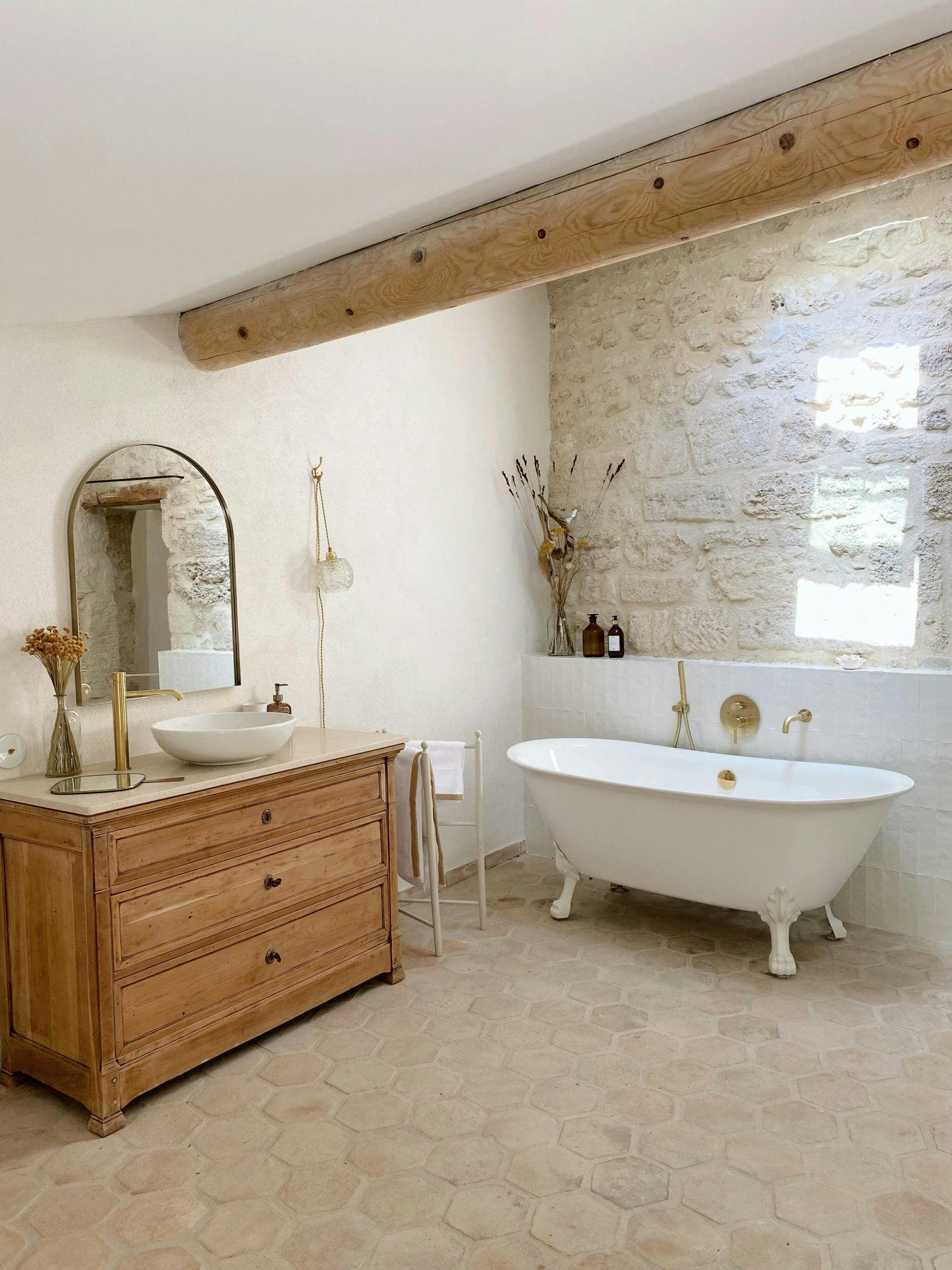 Bathroom with free-standing bathtub, wooden cabinet and washbasin, stone walls and beam