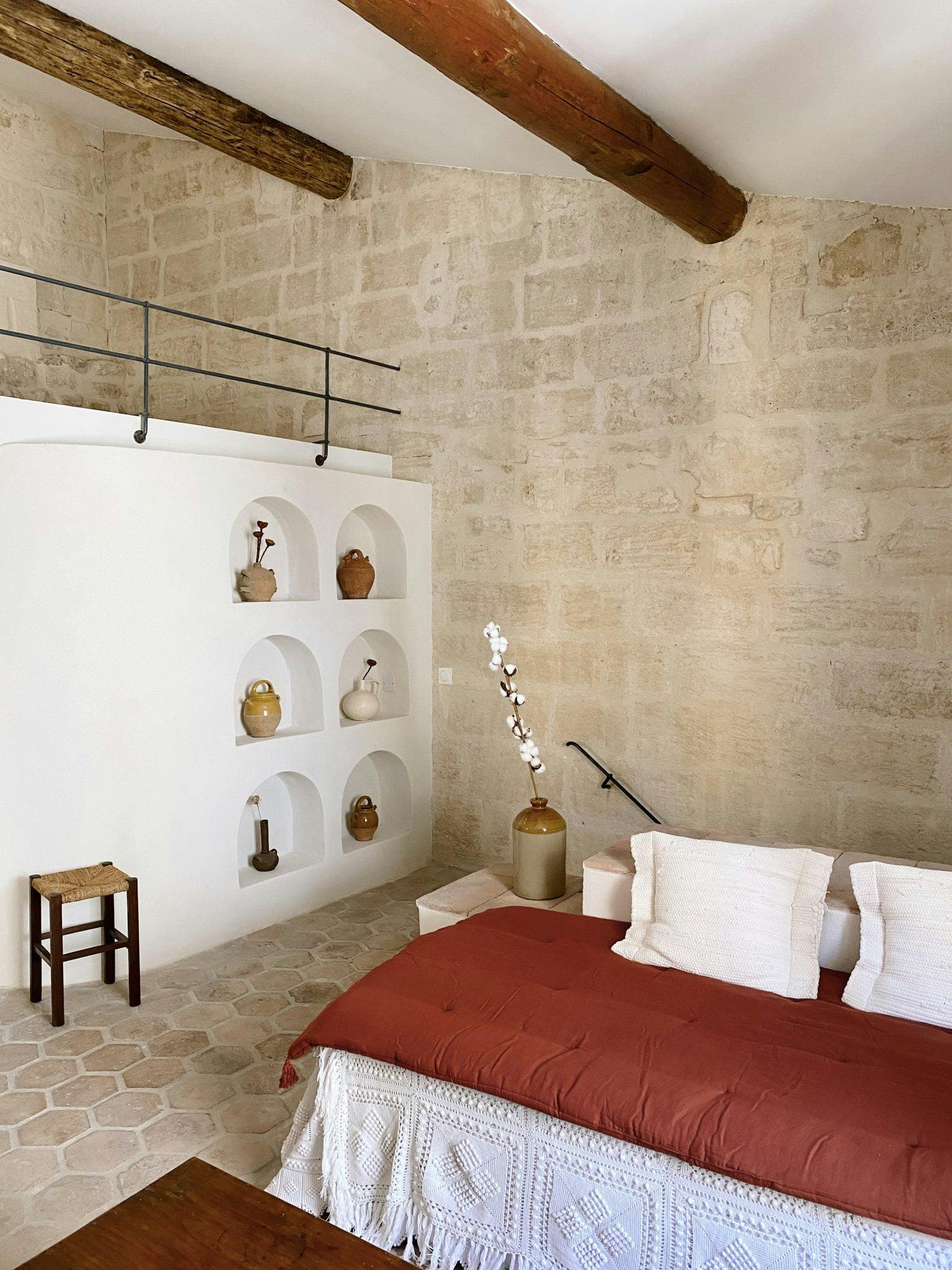 Belle chambre joliment décorée : murs en pierre, niche avec objets et hauteur sous plafond
