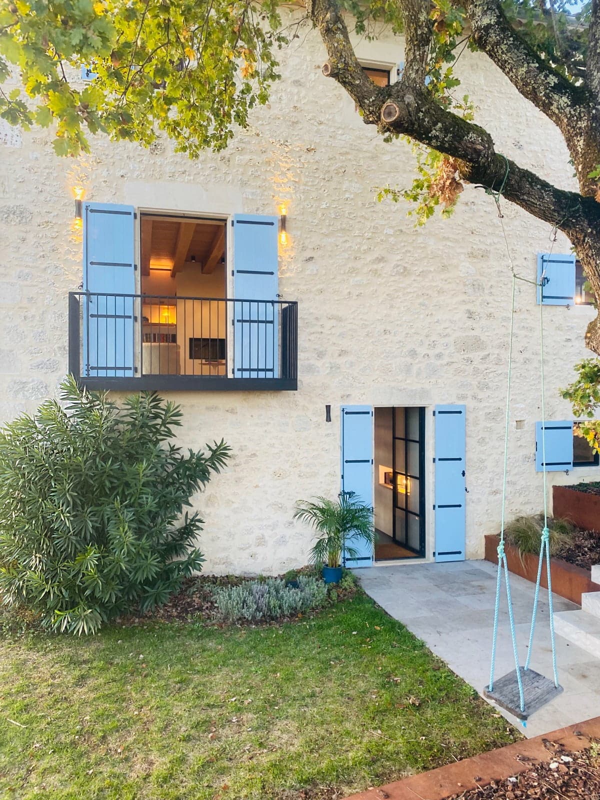 View of the stone house with its blue shutters and rope swing