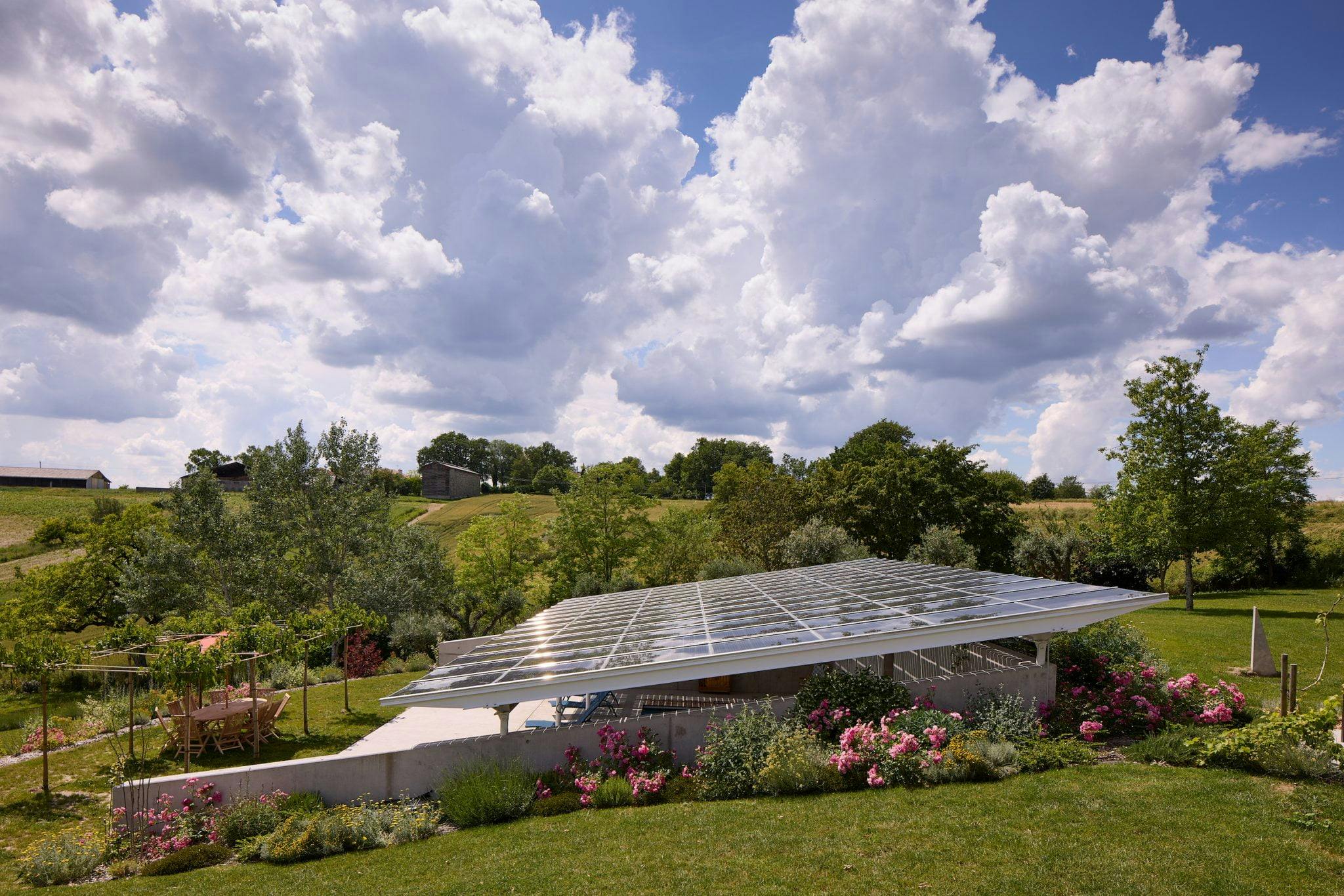 Vue sur le auvent de la piscine constitué de panneaux solaires, le jardin autour