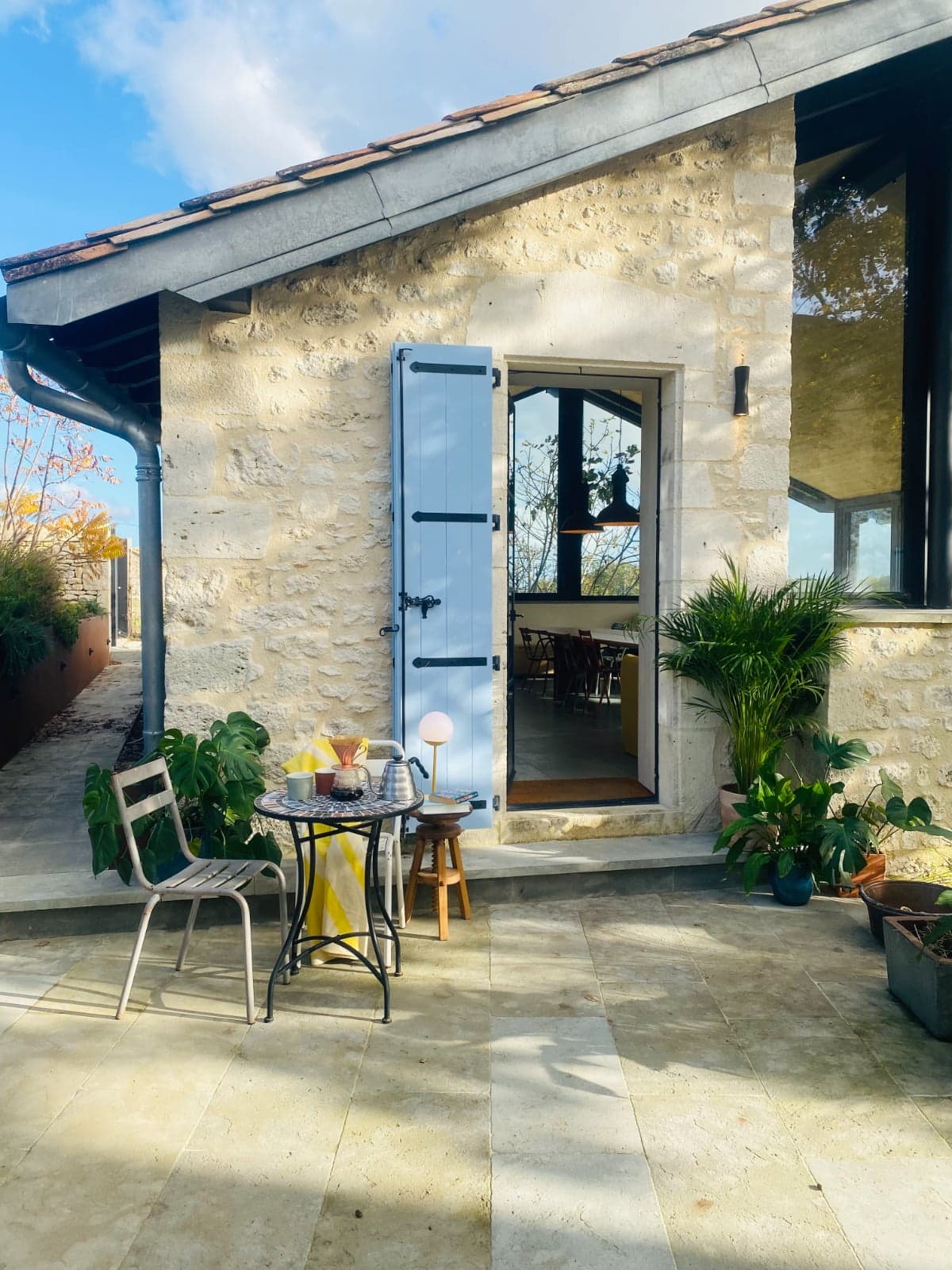 Terrace, wrought-iron table and two chairs in front of the house with its stone walls and blue shutters