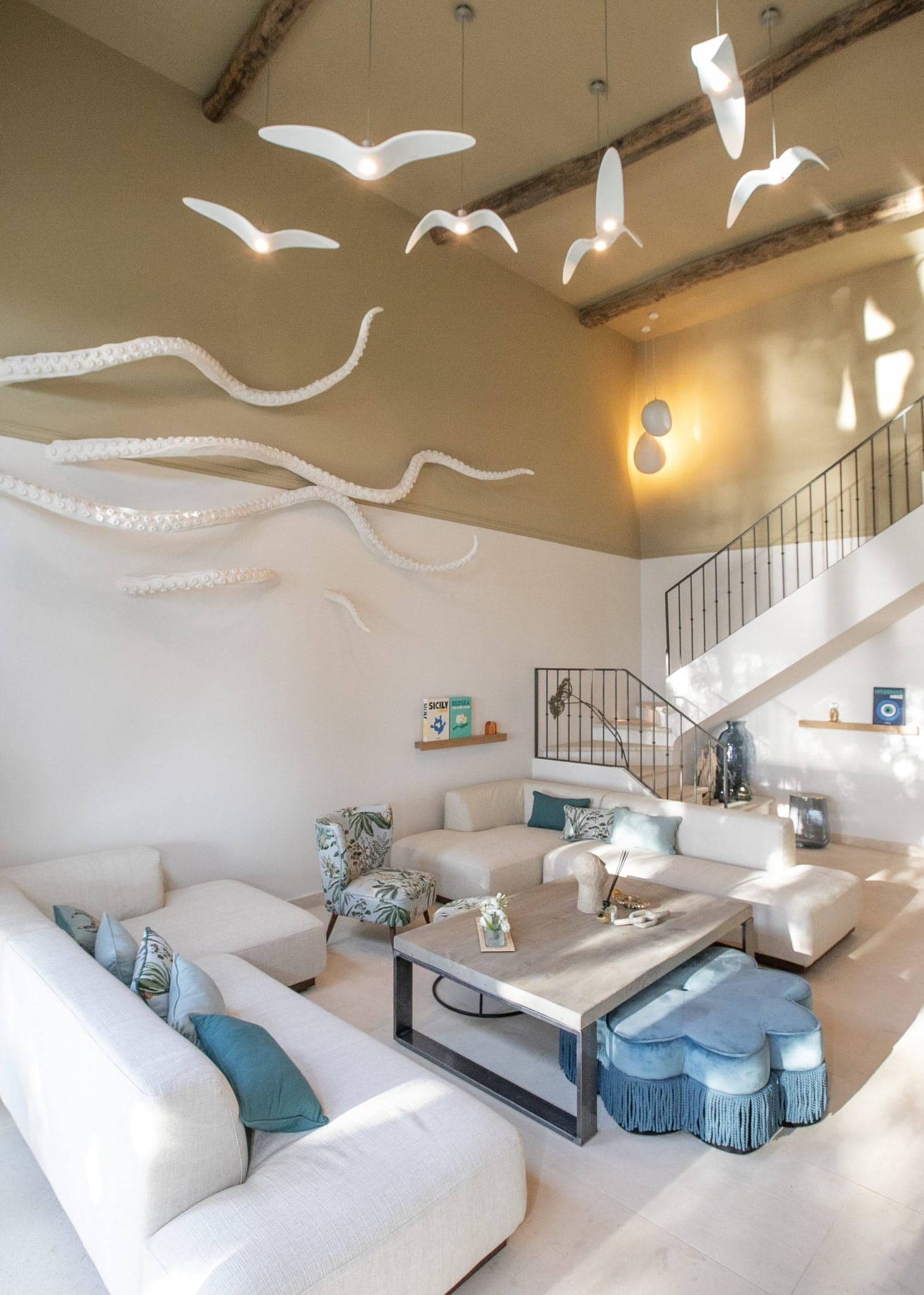 Living room decorated with an octopus sculpture on the wall, high ceilings, white sofas and hanging birds