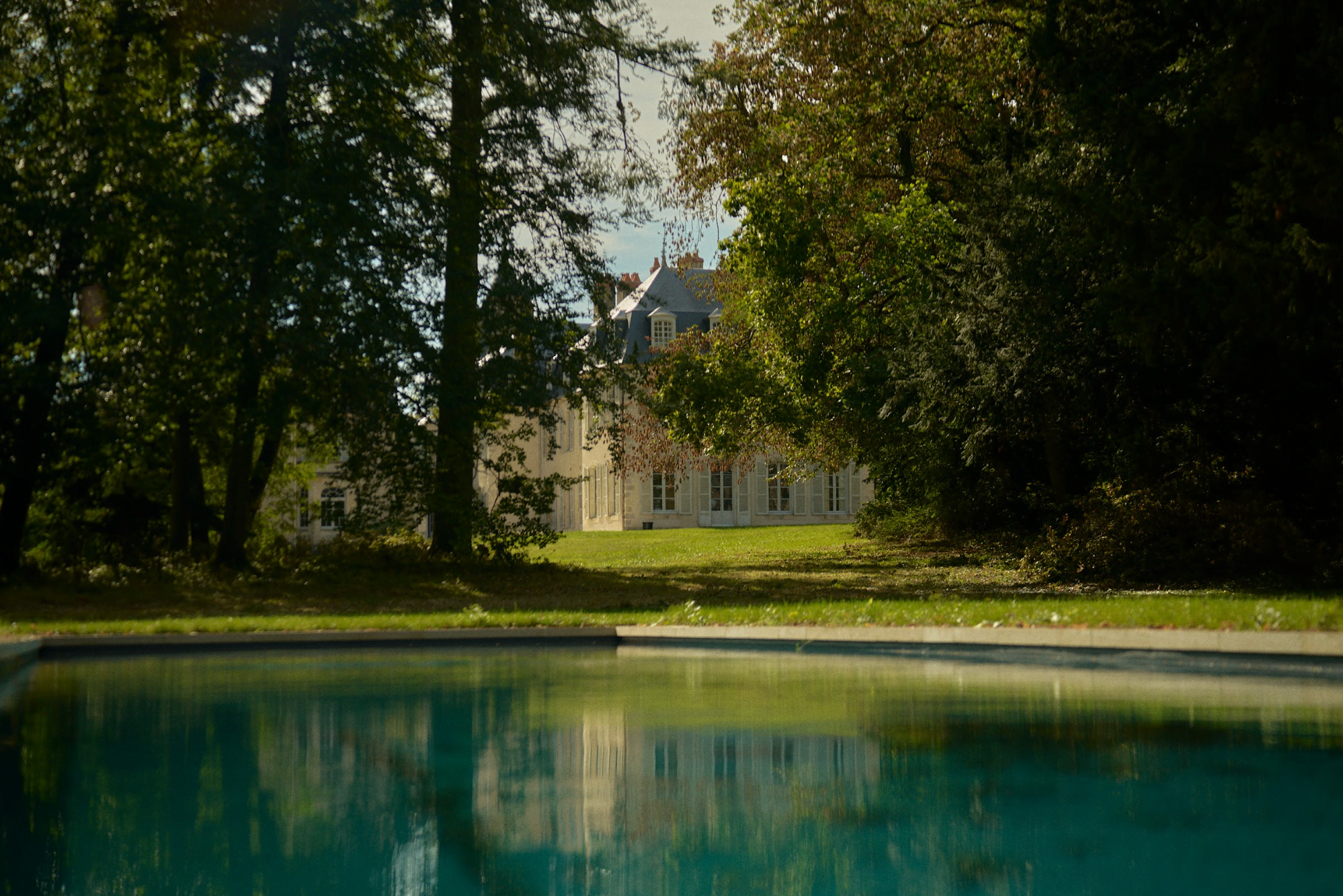 La piscine du Château de Thauvenay au milieu de la pelouse et des arbres