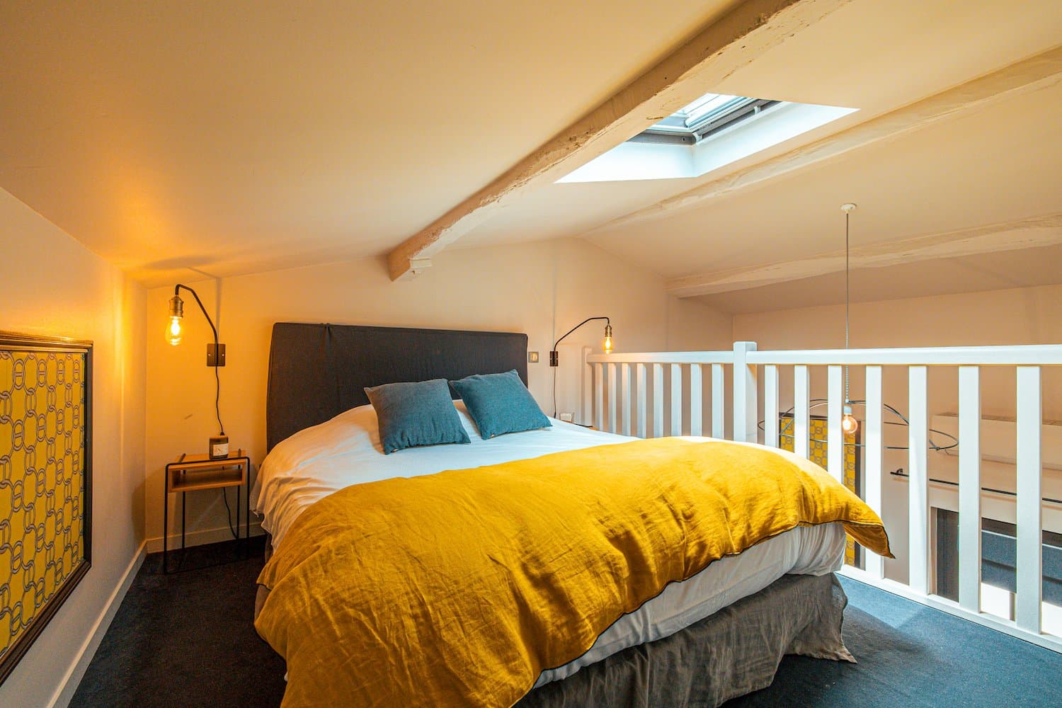 Chambre nichée sous les toits ouvert par un velux, draps jaunes et bleus