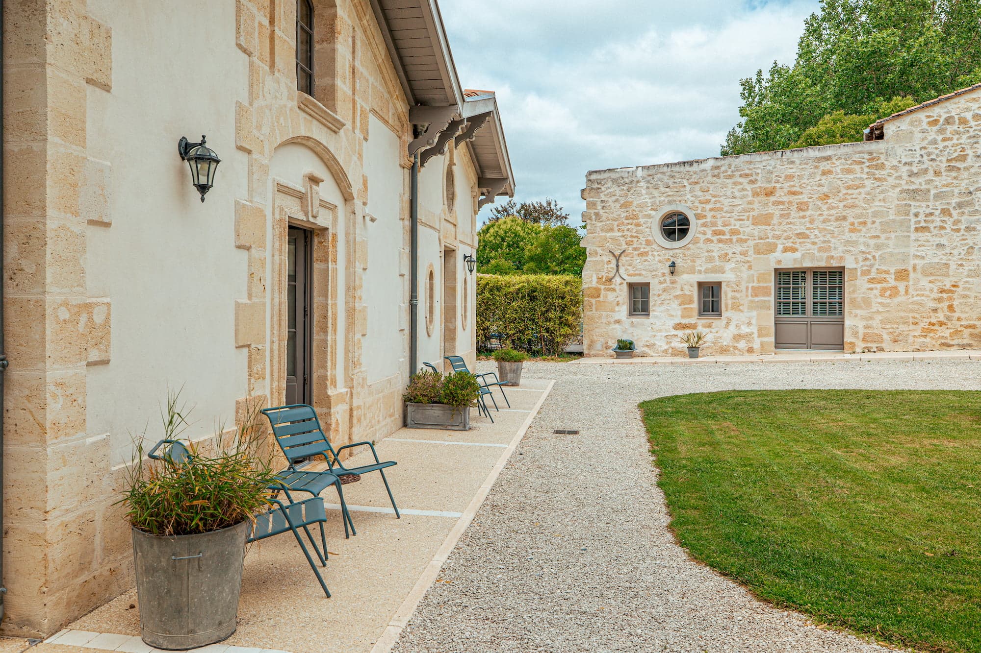 L'arrière de la maison et sa façade en pierre, deux chaises design et un bord de pelouse