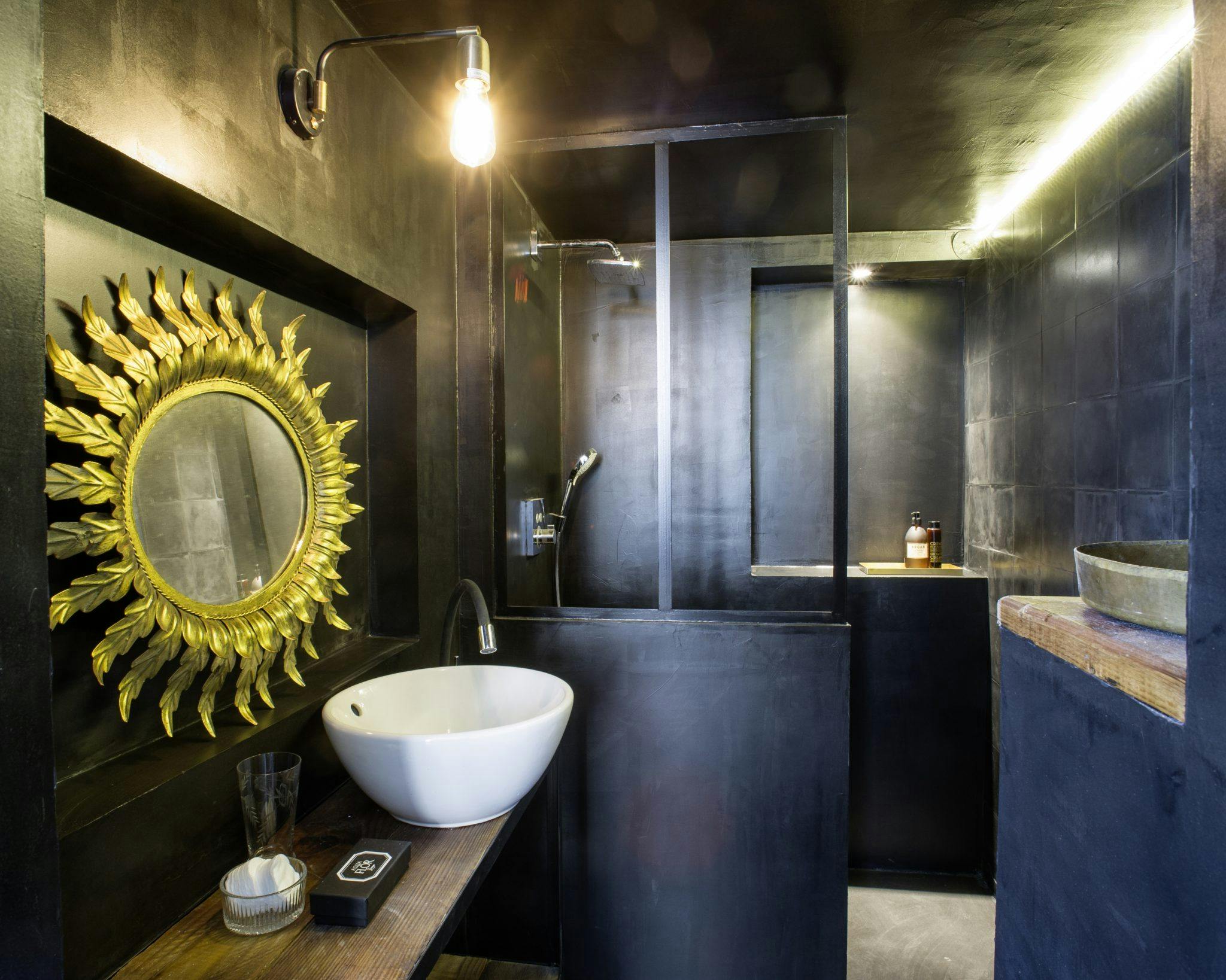 Detail of the bathroom with black walls, glass bay window, and golden mirror.