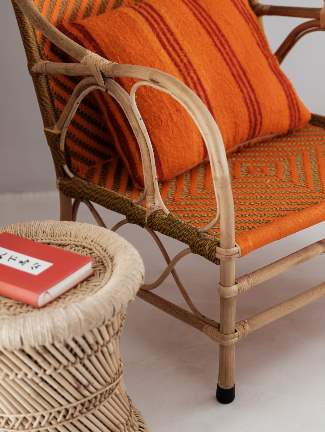 Detail of a rattan armchair and orange cushion.