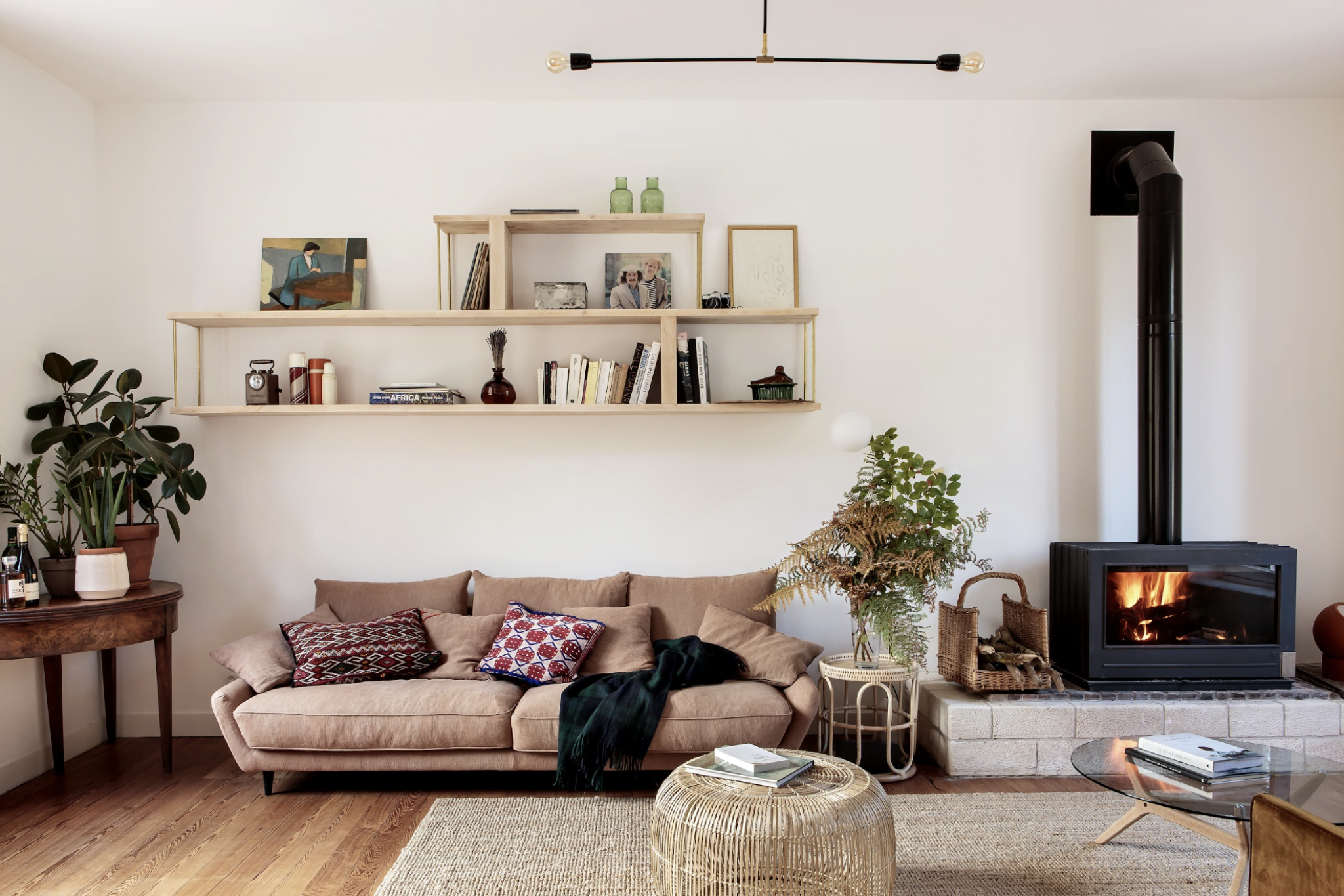 The Riverside House living room: pink sofa, white walls, wall-mounted bookcase, rattan rug.