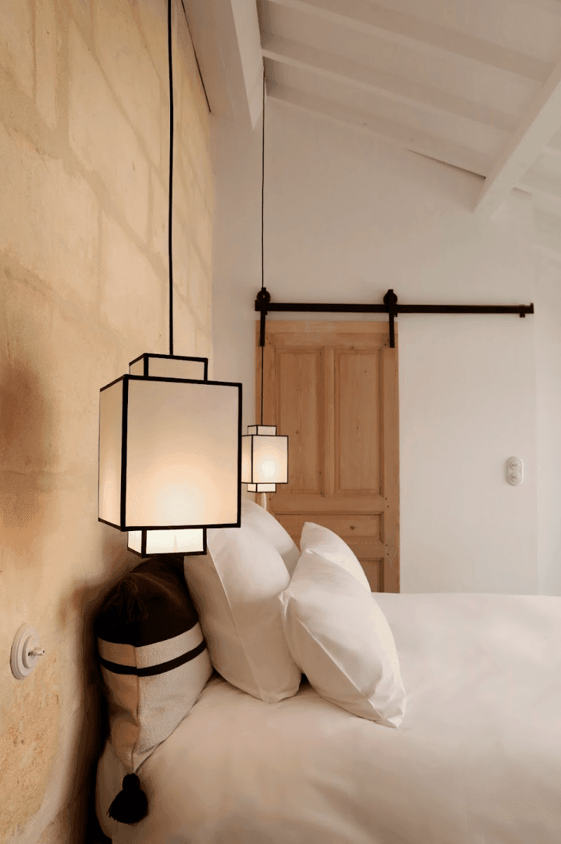 The elevated bedroom: white sheets, hanging lights next to the bed