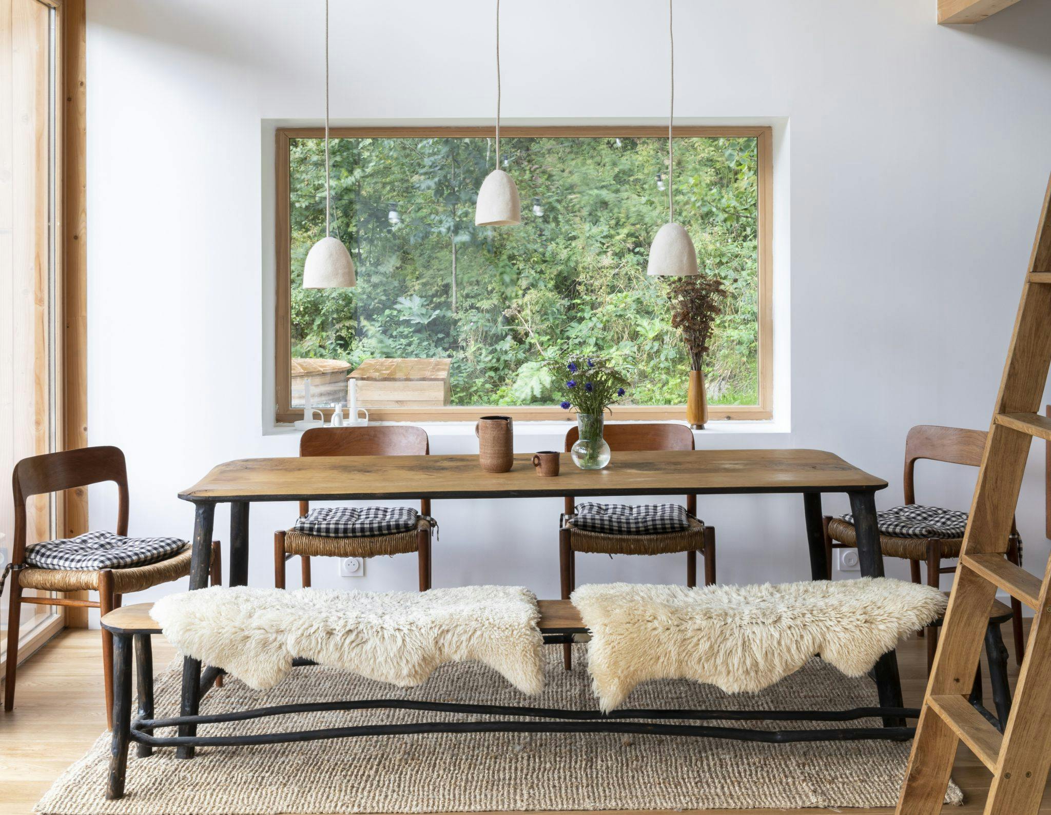 The wooden dining table of La Maison Refuge, the chairs, and the sheepskin fur throws