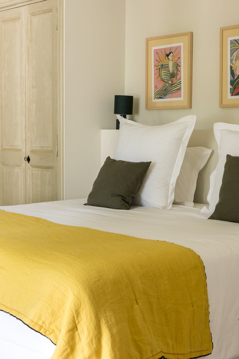 Détail de l'une des chambres du Mas le Gaudre : dessus de lit jaune, peintures contemporaines au mur