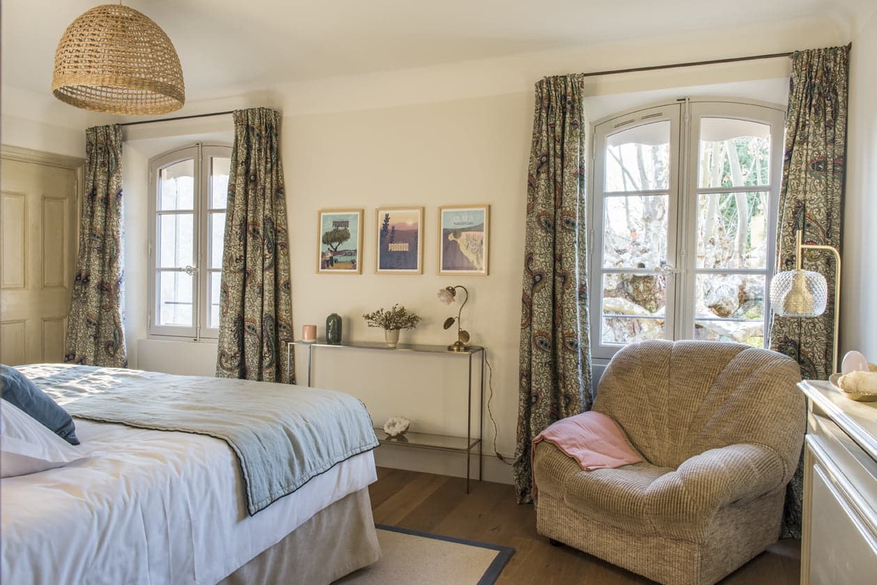 L'une des chambres du Mas le Gaudre aux couleurs pastels : fauteuil, rideaux Pierre Frey, dessus de lit bleu ciel