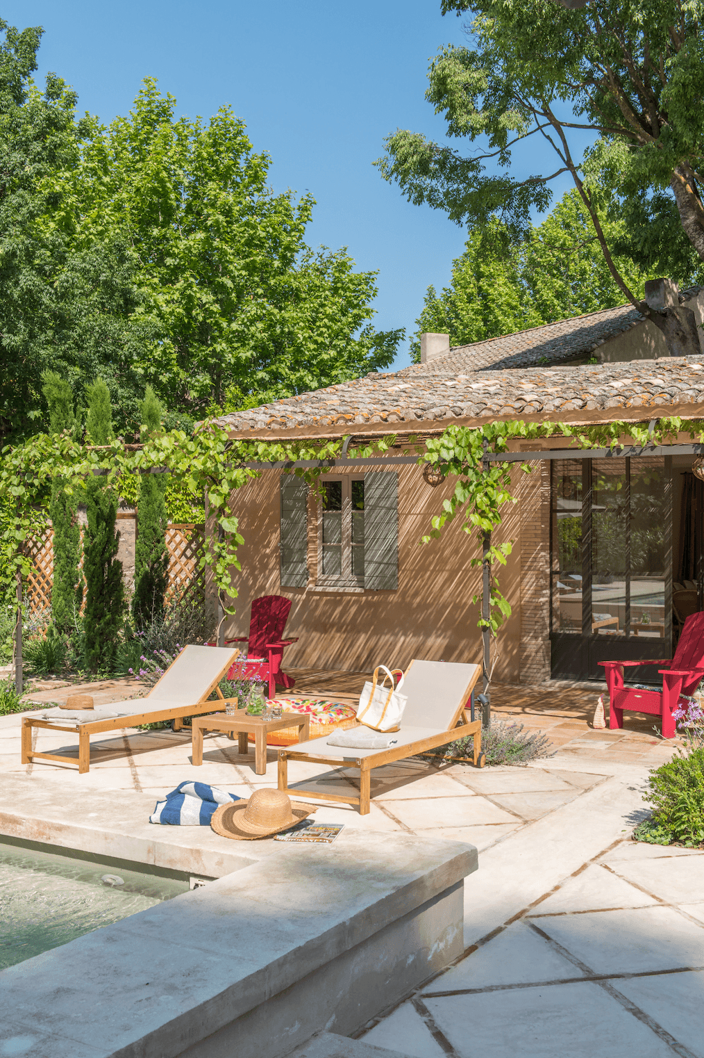 Les transats au bord de la piscine devant la petite maison et la plante grimpante