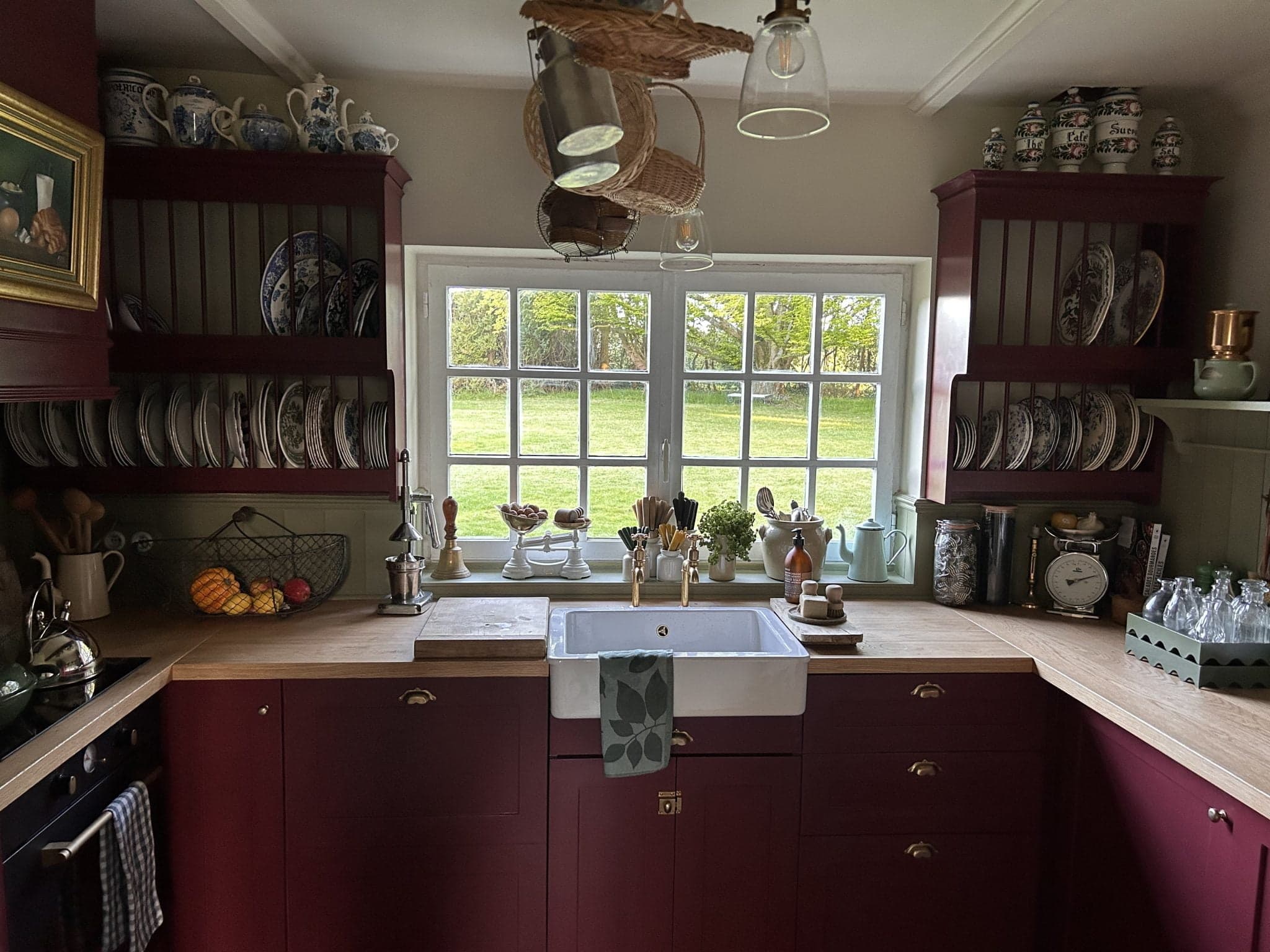 The kitchen of La Roquerie: red furniture, wood, and a window overlooking the garden