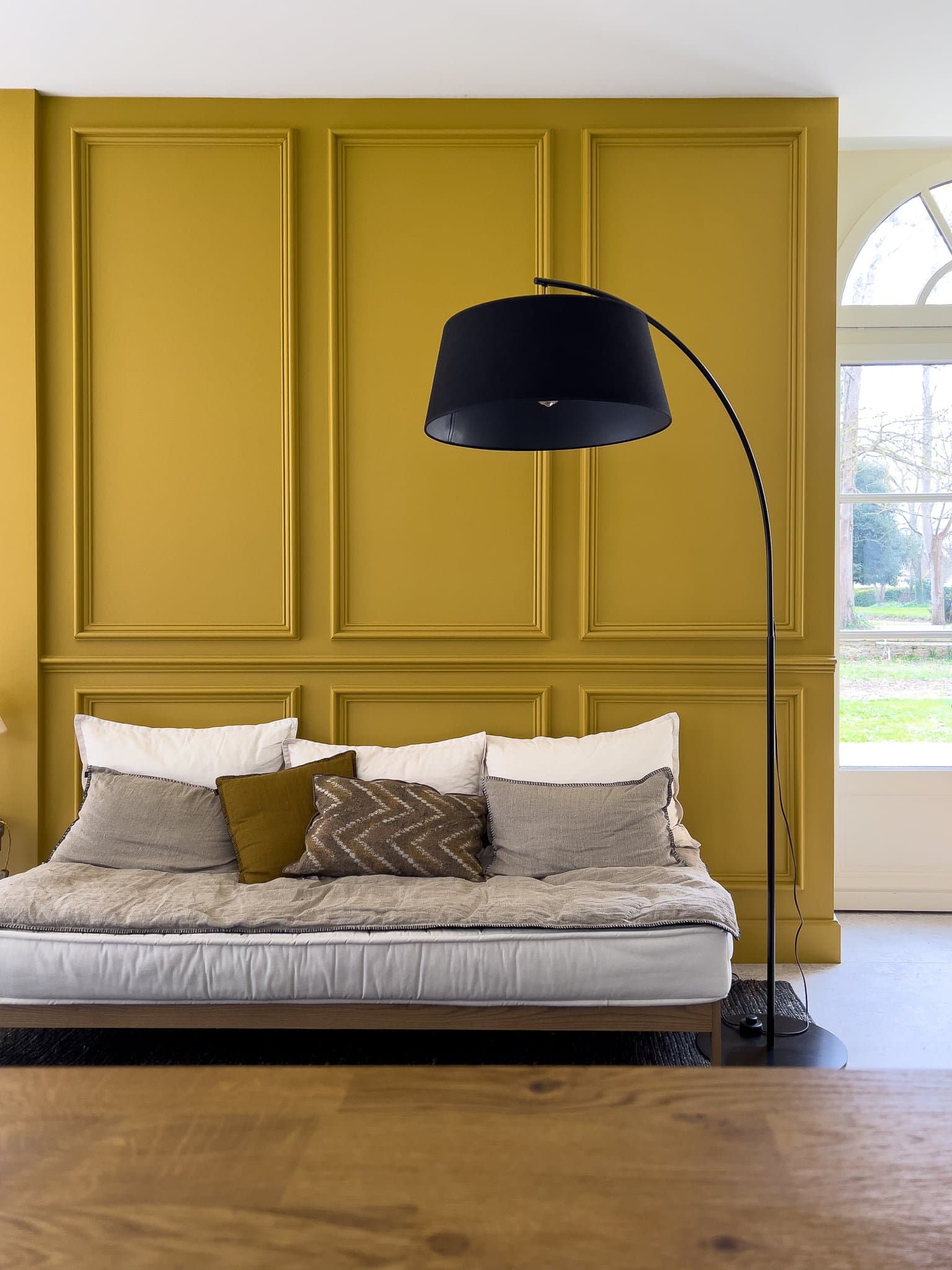 Boiseries sur le mur jaune curry, canapé et lampe noire