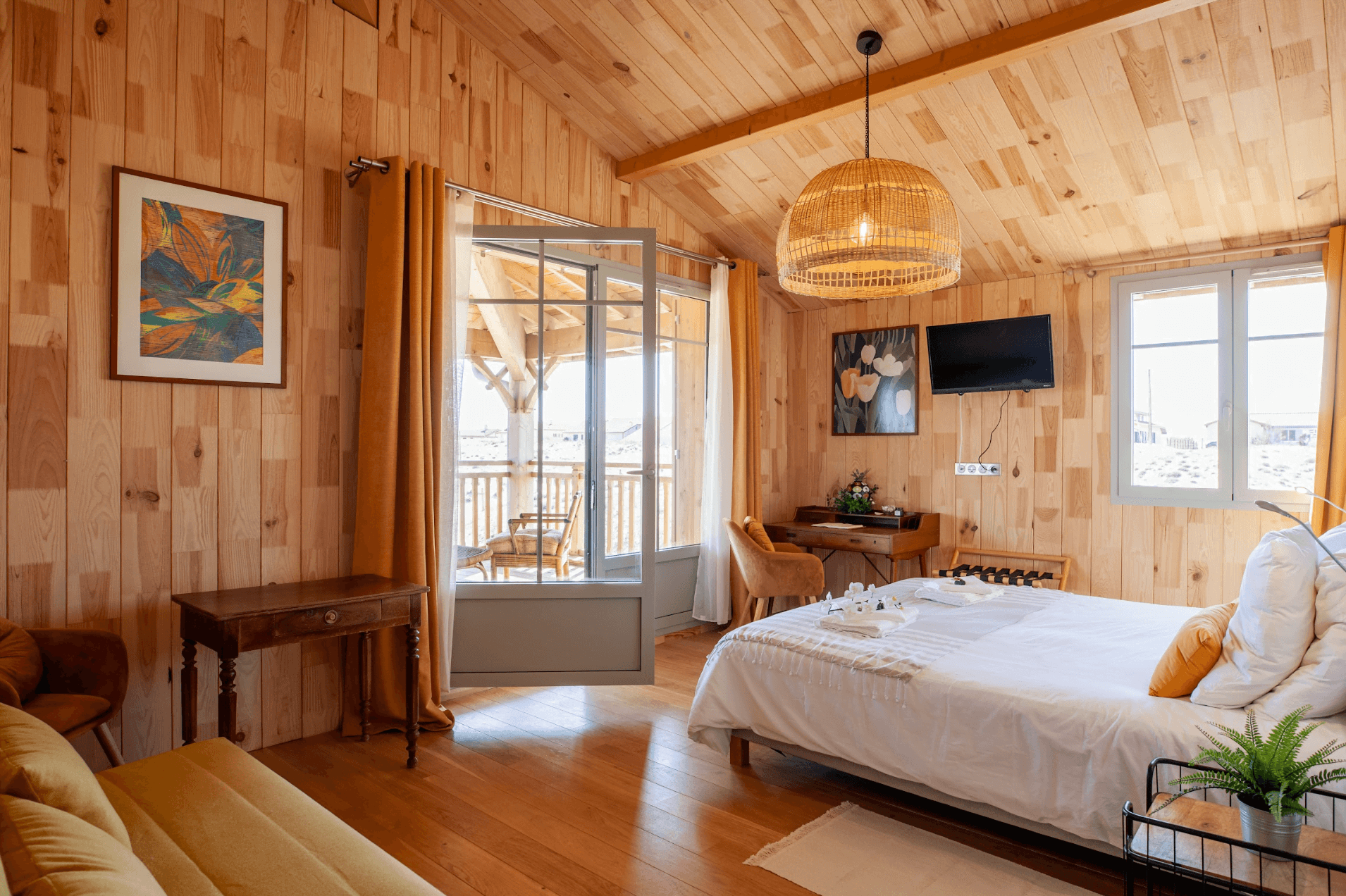 Chambre avec lit double, linge de lit blanc, murs et poutres en bois, baie vitrée