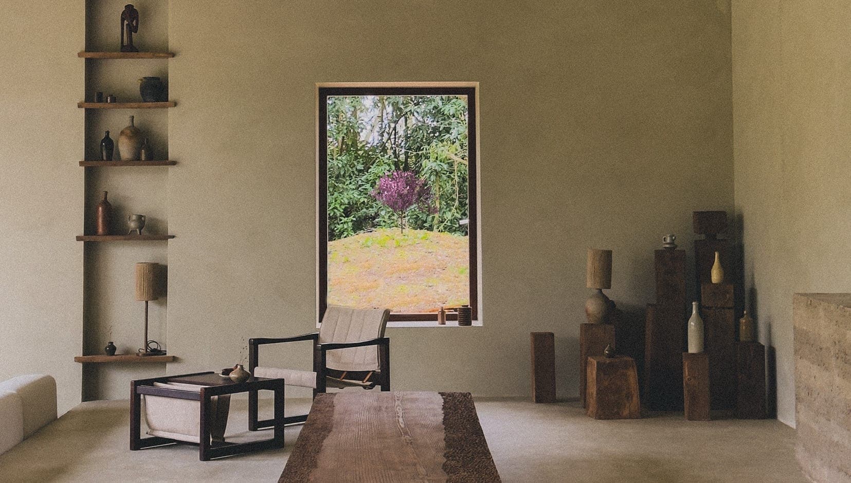 Minimalist living room with neutral tones. A large window showcases a green landscape with a single purple-leaved tree. The room features wooden furniture, a tall corner shelf with décor, and earthy accents.