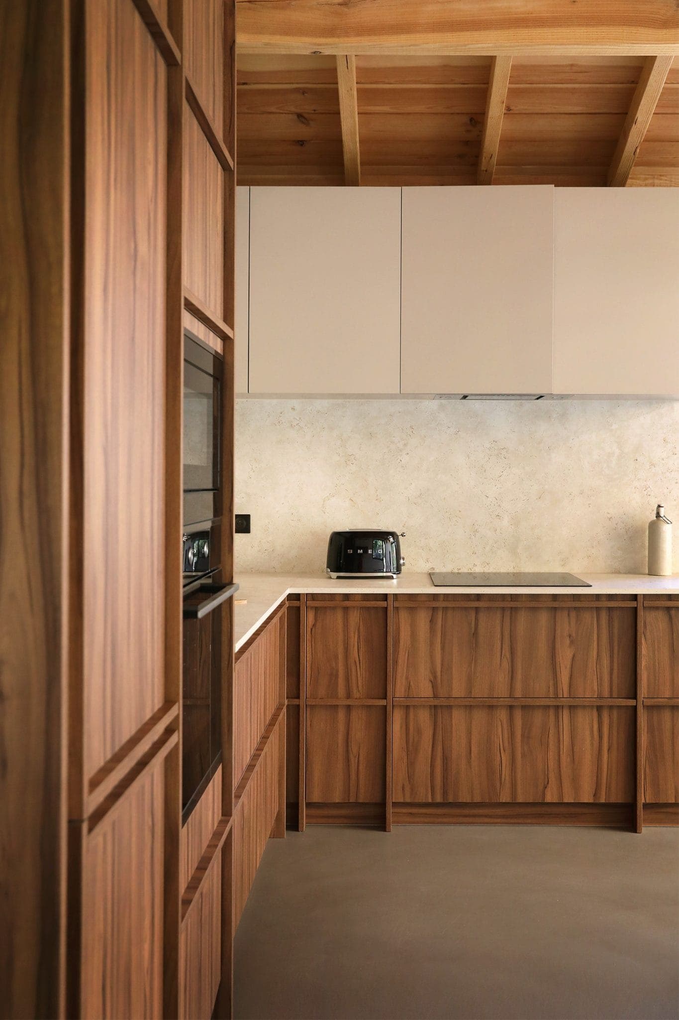 Modern kitchen with wood cabinets, beige upper cabinets and beige backsplash. A black toaster and white paper towel holder are placed on the countertop. The ceiling features exposed wood beams.