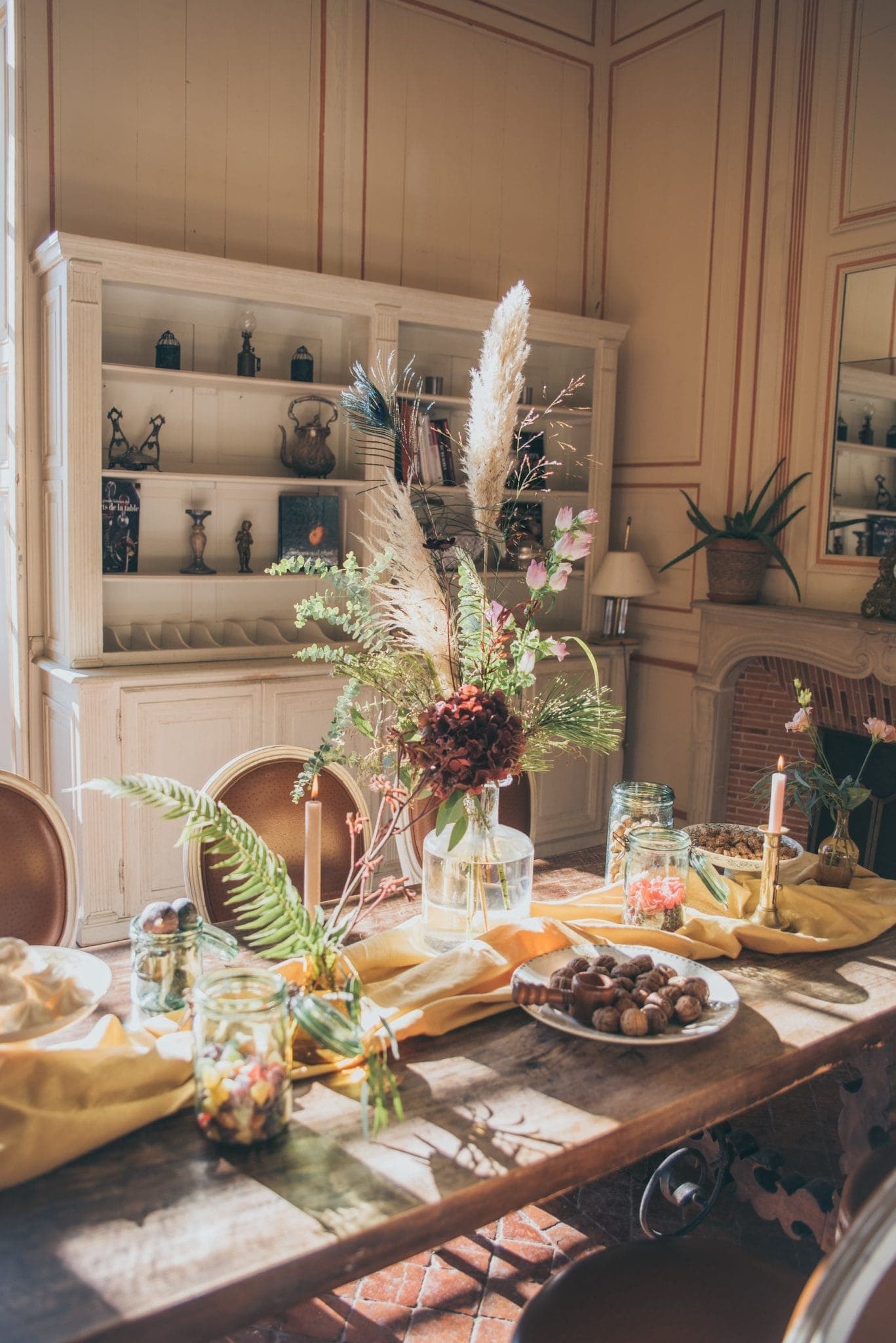 A beautifully set dining table with floral arrangements and candles. The table is covered with a pink tablecloth and features decorative plates and glassware, creating an elegant and welcoming atmosphere.