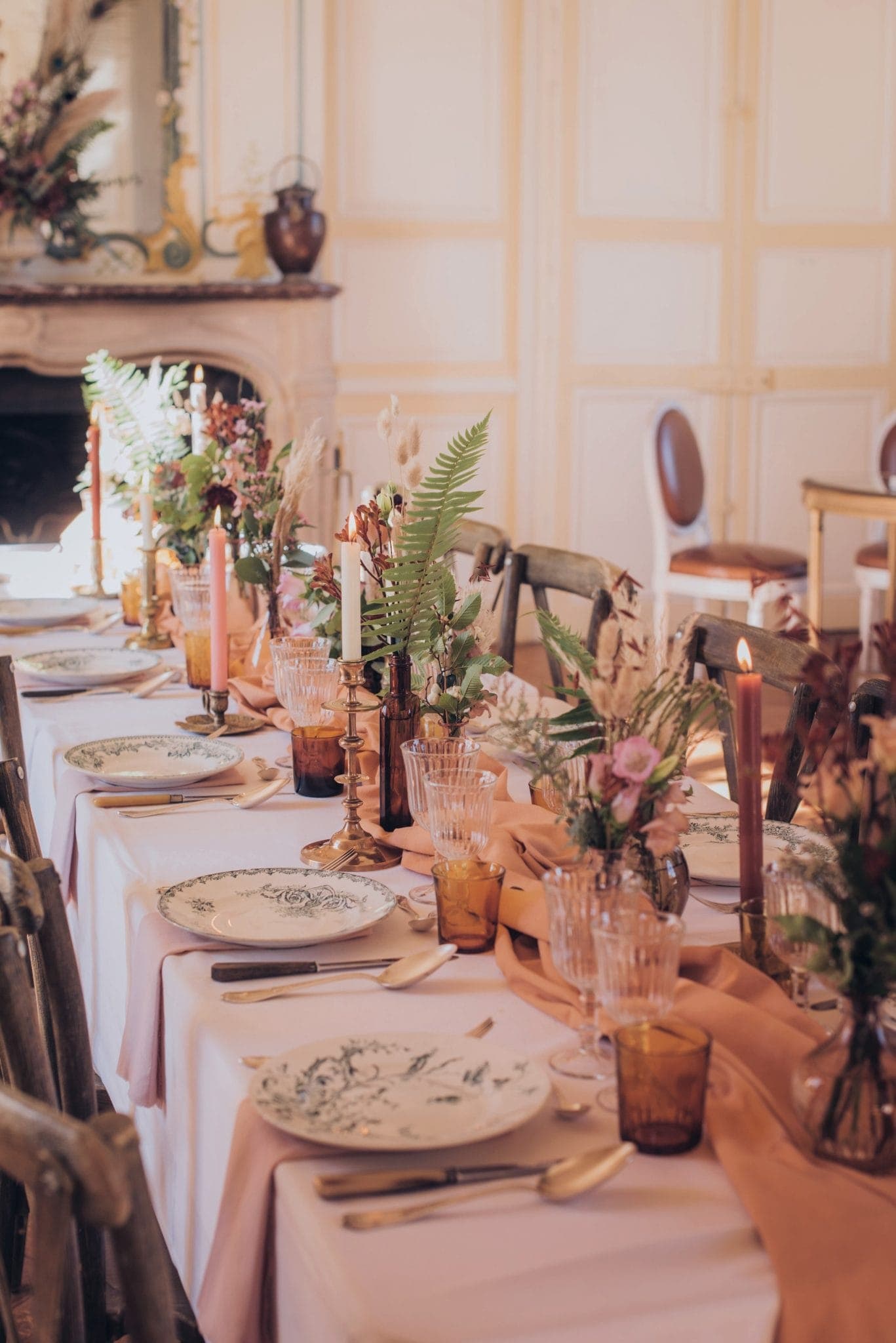 A beautifully set dining table with floral arrangements and candles. The table is covered with a pink tablecloth and features decorative plates and glassware, creating an elegant and welcoming atmosphere.
