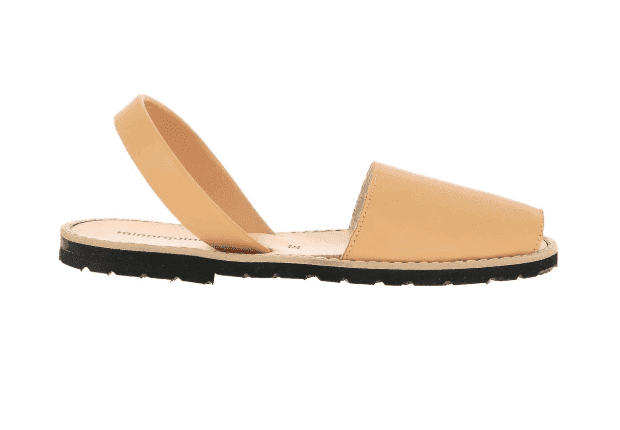 Une sandale en cuir beige avec une semelle plate noire est présentée. Elle présente un talon ouvert et un bout fermé, avec une seule sangle autour du talon pour le maintien. La sandale est présentée sur un fond blanc uni.
