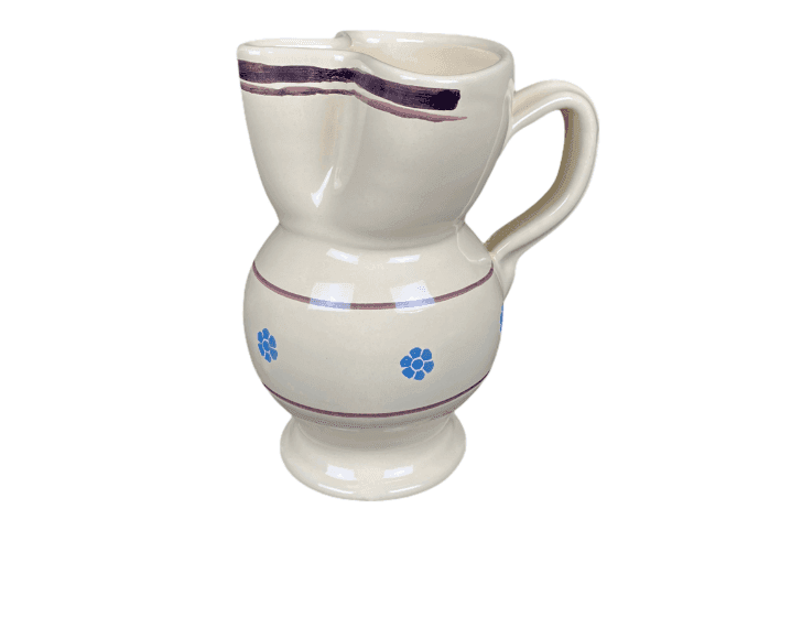 Pichet en céramique de couleur crème avec une base ronde et une anse. Il présente une ligne sombre ondulée près du haut et des motifs de fleurs bleues au milieu. Le bec verseur est large et le pichet a une finition brillante.
