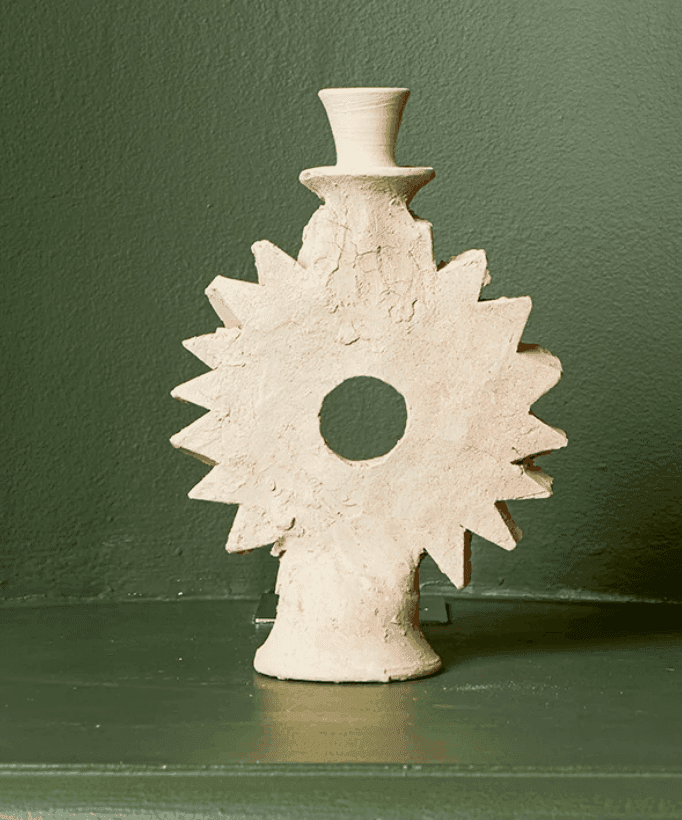 Une sculpture en argile en forme d'étoile ou d'engrenage et un centre creux, comportant un petit sommet cylindrique, sur fond vert pâle.