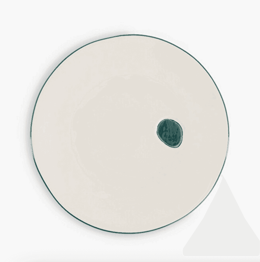 Assiette ronde en céramique blanche, de forme légèrement irrégulière, ornée d'un petit cercle bleu sarcelle foncé près du bord. Le bord est fin et le fond est blanc uni.