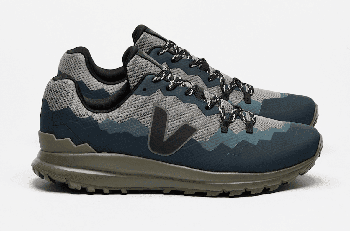 Une paire de baskets élégantes au design camouflage dans des tons bleus et gris. Elles sont dotées de lacets complexes et d'une semelle robuste vert olive, sur fond blanc uni.