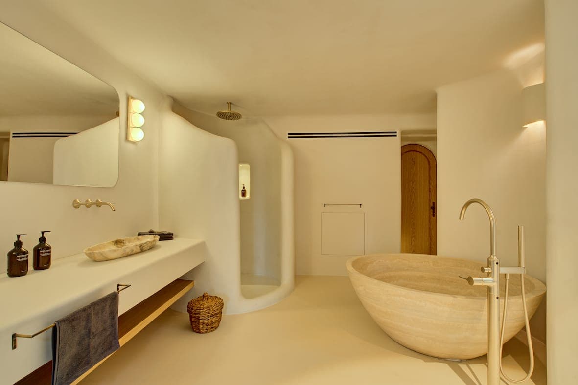Minimalist bathroom with smooth stone bathtub and curved open shower. The vanity features a large mirror, warm lighting and modern fixtures. Neutral tones and natural materials create a soothing atmosphere.