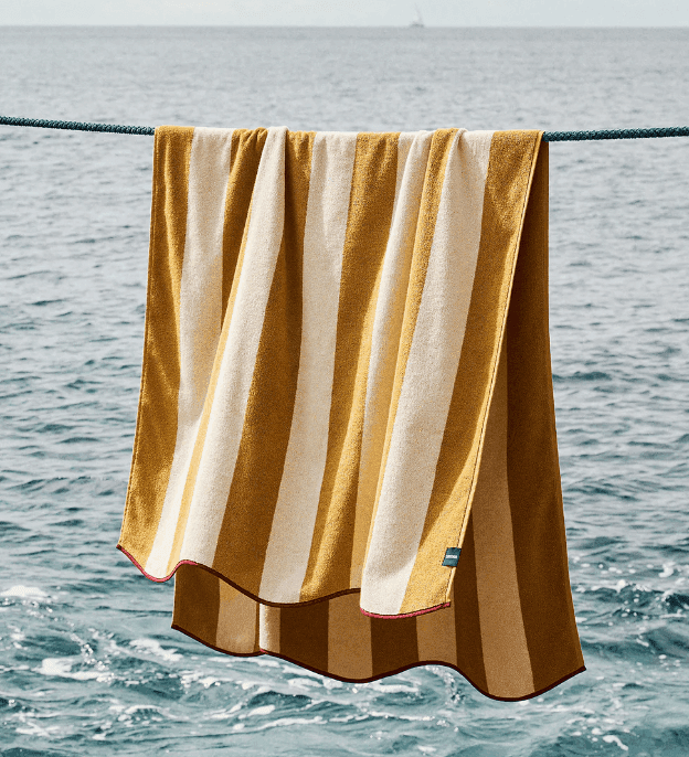 Une serviette à rayures dorées et blanches est suspendue à une corde à linge avec l'océan et de douces vagues en arrière-plan par temps clair.