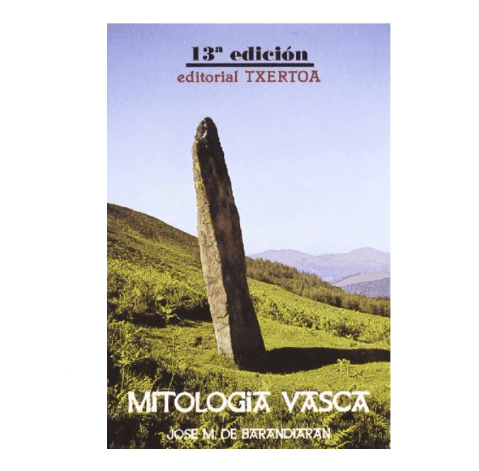 Couverture de « Mitología Vasca » de José M. de Barandiaran. On y voit un menhir dressé dans un champ herbeux, avec des collines ondulantes et un ciel dégagé en arrière-plan. Le texte indique qu'il s'agit de la 13e édition de l'ouvrage, édité par Editorial Txertoa.