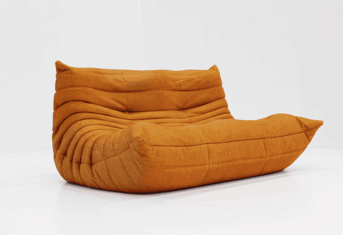 Un canapé moderne, orange et bas, au design doux et ondulé, repose sur un fond blanc. Son allure unique et moelleuse se caractérise par des coutures horizontales incurvées et une atmosphère chaleureuse et accueillante.