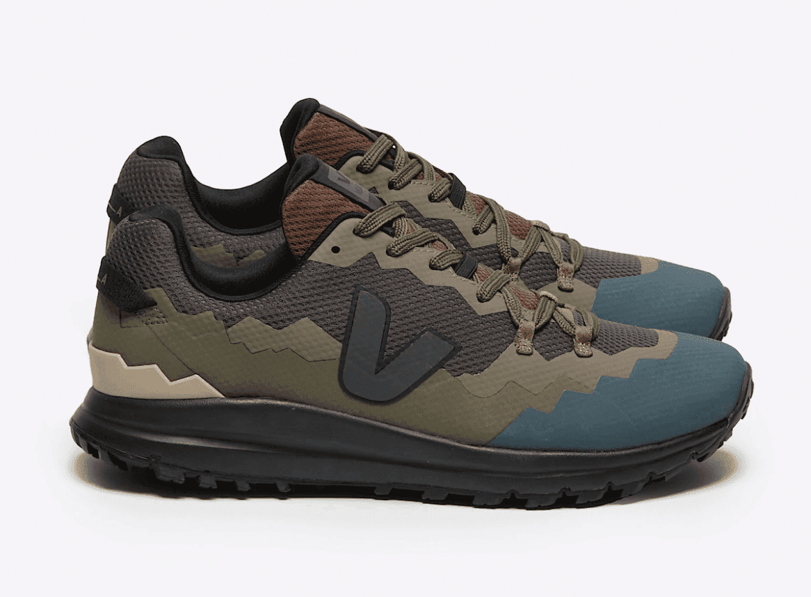 Une paire de baskets de sport à motif zigzag aux tons terreux de vert, marron et bleu. Elles sont dotées de lacets et de semelles noirs, et arborent un logo « V » bien visible sur les côtés. Elles reposent sur un fond blanc uni.