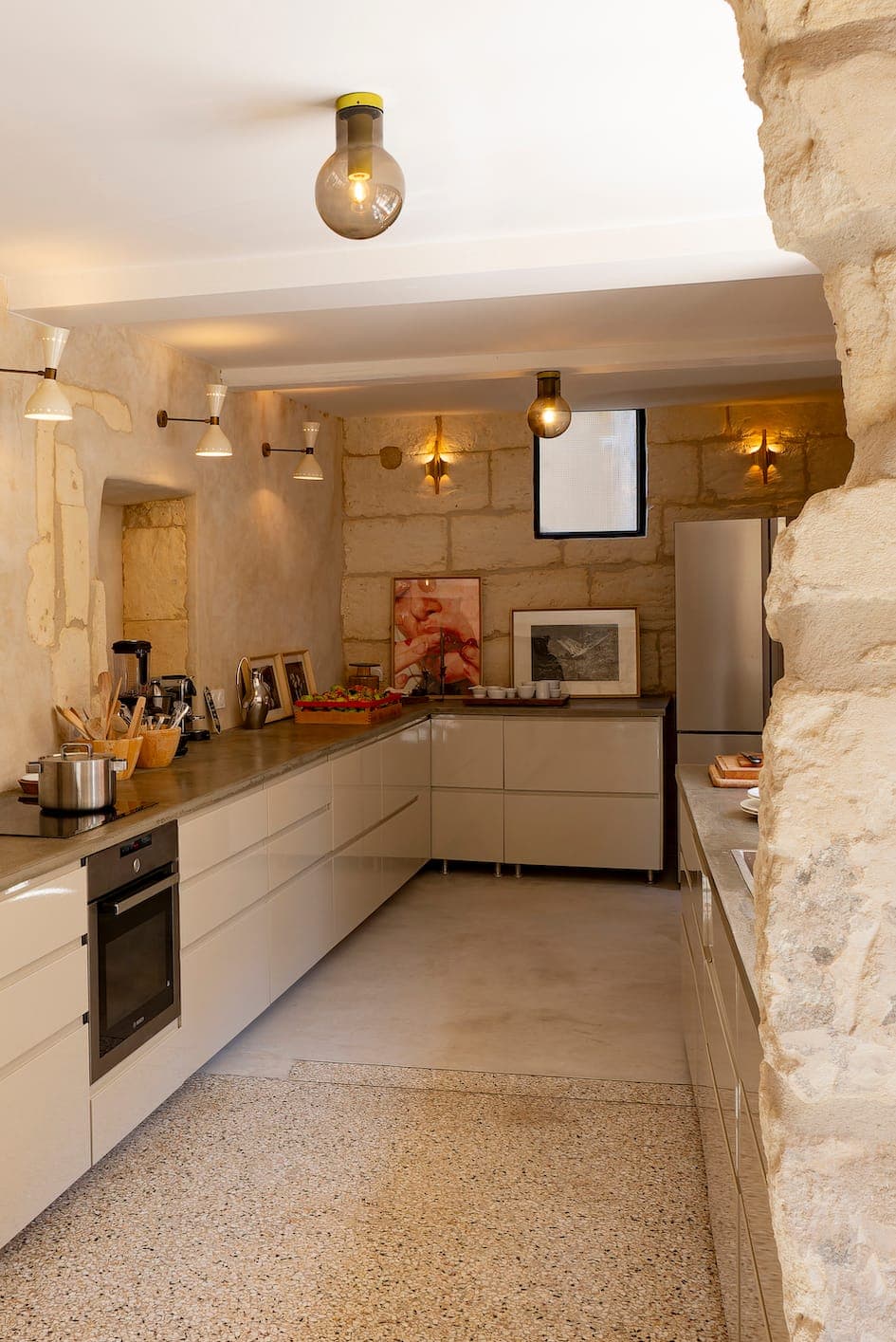 Une cuisine moderne avec murs en pierre, placards lumineux, four encastré, électroménagers de comptoir, œuvres d'art encadrées et réfrigérateur. Un éclairage chaleureux et des textures naturelles créent une atmosphère chaleureuse et accueillante.