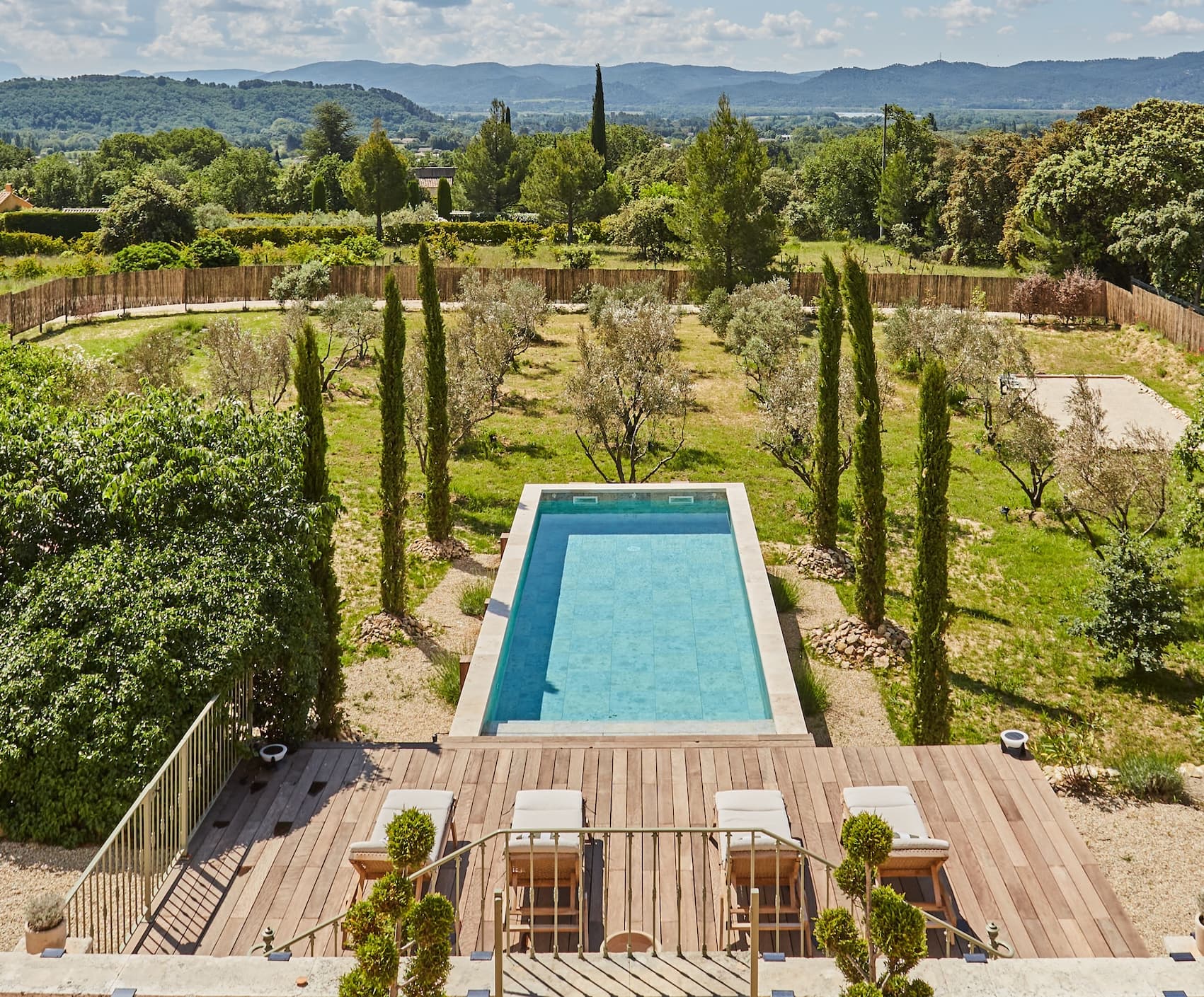 Une vue panoramique depuis la terrasse donnant sur une piscine, des cyprès et des montagnes au loin.