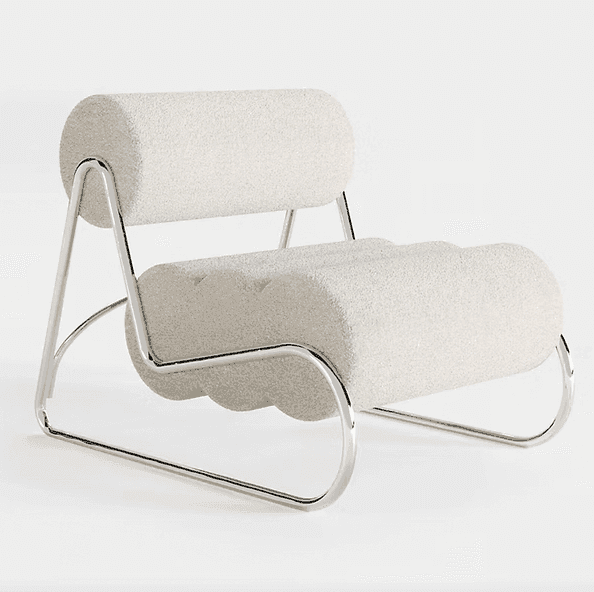 Un fauteuil moderne avec une structure tubulaire chromée et un revêtement crème moelleux et arrondi sur l'assise et le dossier, sur un fond clair uni.