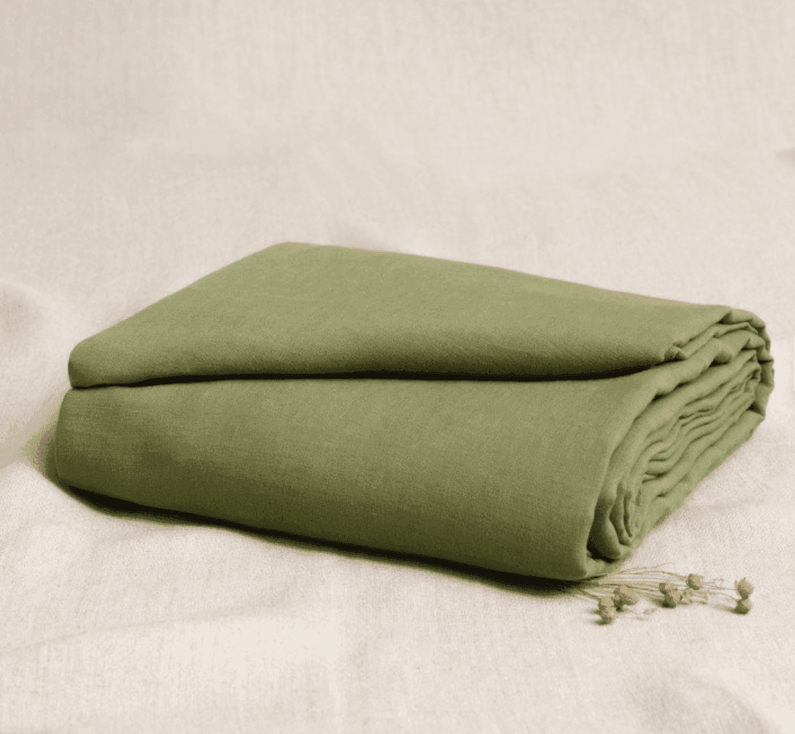 Un drap vert olive soigneusement plié repose sur une surface en tissu beige clair, avec quelques petites fleurs séchées placées à côté.