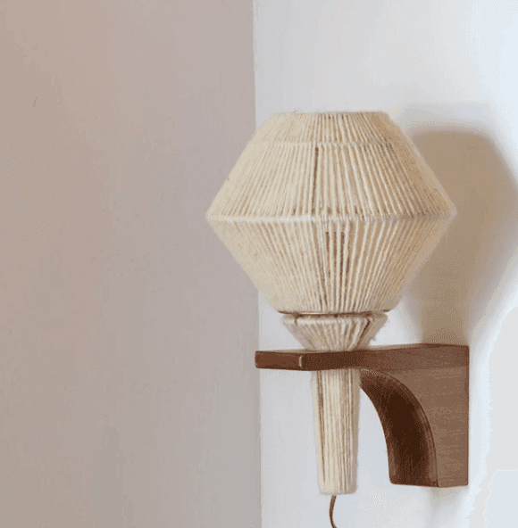 Applique murale avec abat-jour géométrique couleur crème gainé de fil et support en bois, fixée sur un mur blanc. Cette lampe affiche un style moderne et artisanal.