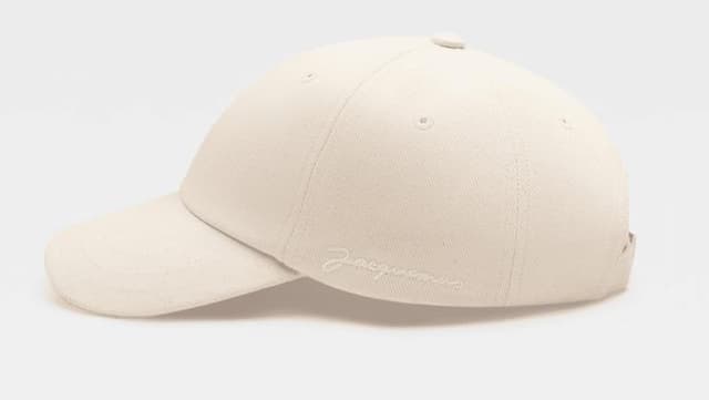 Casquette de baseball beige avec le logo "Jacquemus" brodé sur le côté. La casquette a une visière incurvée et se détache sur un fond blanc uni.