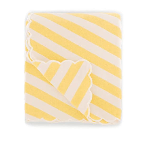 Un couvre-lit plié avec des rayures diagonales jaunes et blanches. Elle présente un design de bord festonné, révélant un motif similaire sur le dessous. La couverture est soigneusement pliée, mettant en valeur sa palette de couleurs vives et sa bordure unique.