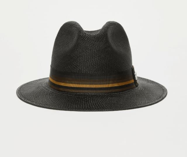 Un chapeau fedora noir à large bord et à bande rayée colorée à la base. Cette bande présente des dégradés de vert, de marron et de jaune. Le fond est uni et neutre.