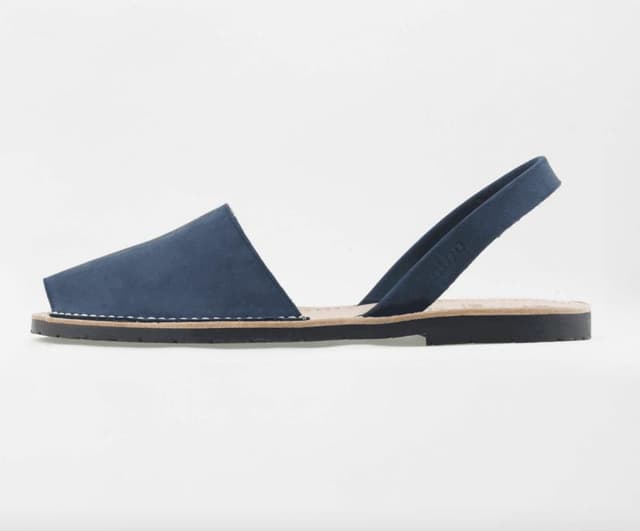 Sandale bleu foncé à bout ouvert et bride arrière. Semelle plate noire et surpiqûres apparentes. Elle se présente sur un fond blanc uni.