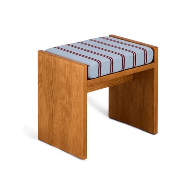 Un tabouret en bois moderne avec des panneaux latéraux plats et un siège rembourré recouvert de tissu bleu clair à rayures rouge foncé et blanches, sur un fond blanc.